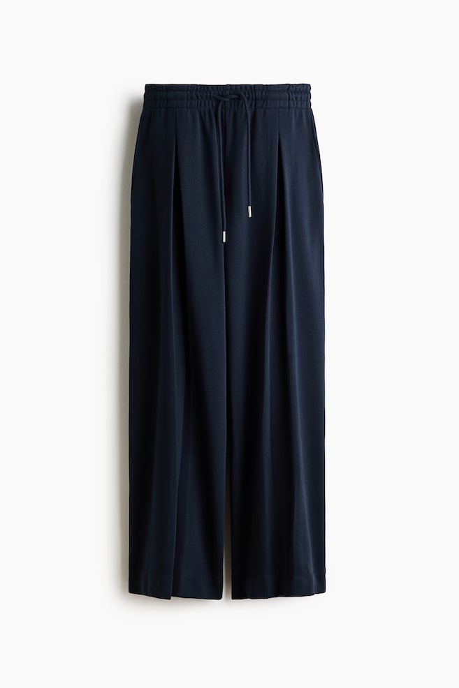 Marineblaue, locker sitzende Hose mit einem elastischen Bund und Kordelzug mit silbernen Enden. Die Hose präsentiert extra lange, weite Beine, die jeweils eine umgekehrte Kellerfalte an der Vorderseite aufweisen, alles gefertigt aus einem leichten Sweatshirtstoff. - 1