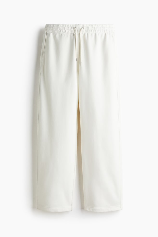 From a front view, cream-colored sweatpants are featuring a loose fit, an elasticated drawstring waist with visible metal-tipped drawstrings, and side pockets. - 1