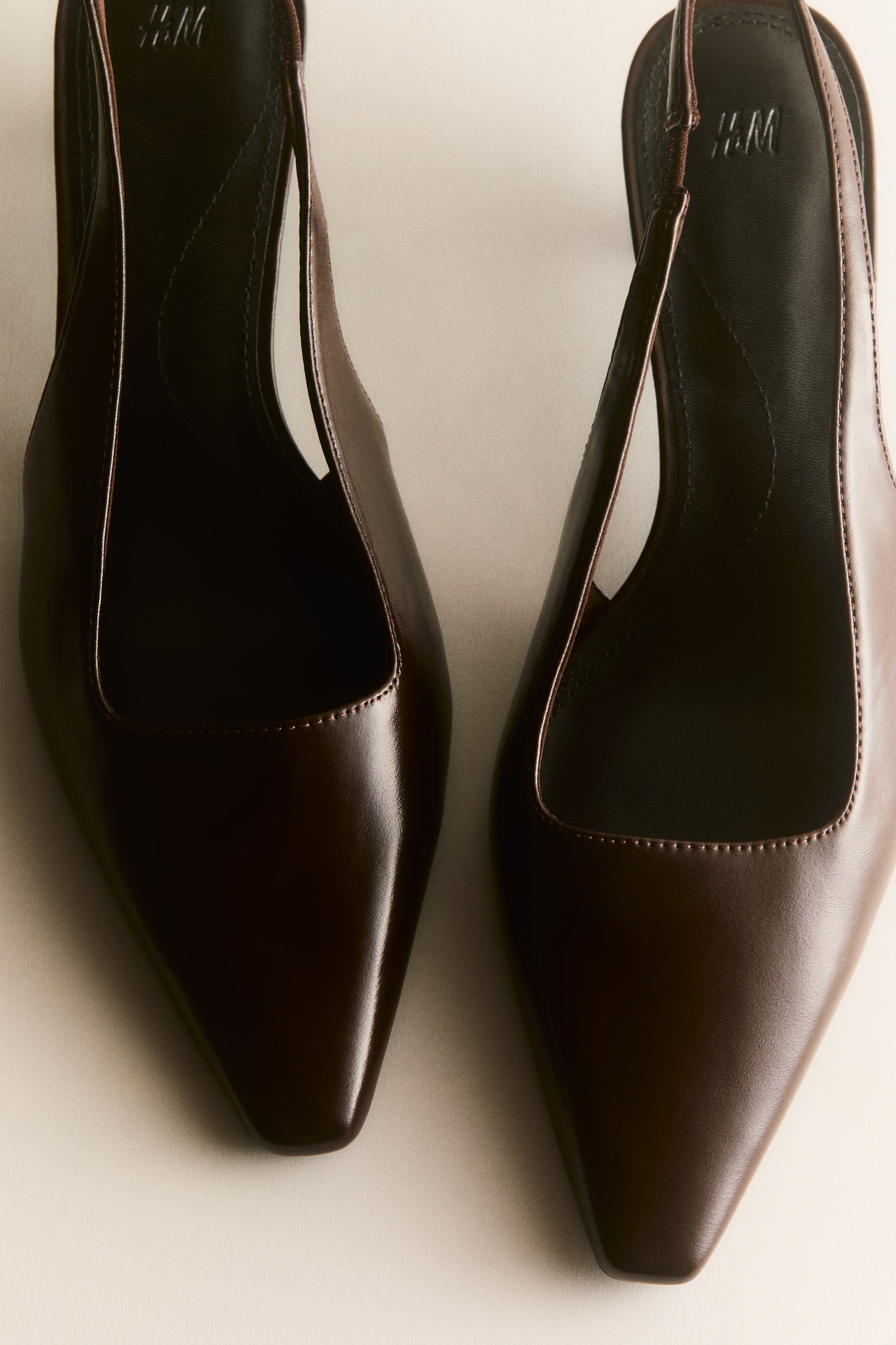 View larger image: Two dark brown slingback heels are displayed side-by-side, each showcasing a pointed toe and a smooth, slightly glossy upper. They feature a slingback strap, fine stitching along the vamp, and an embossed H&M logo visible on the insole.