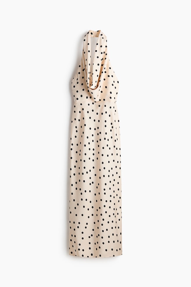 Une robe beige clair à col licou avec des pois noirs est suspendue verticalement, présentant un décolleté drapé en col bénitier et une silhouette droite et longue jusqu'au sol. - 1