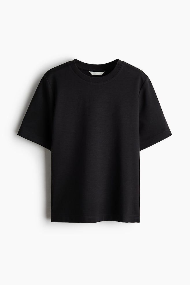 A black cotton jersey T-shirt is shown from the front, featuring a round neck with ribbed trim, short sleeves, and a straight-cut hem. - 1