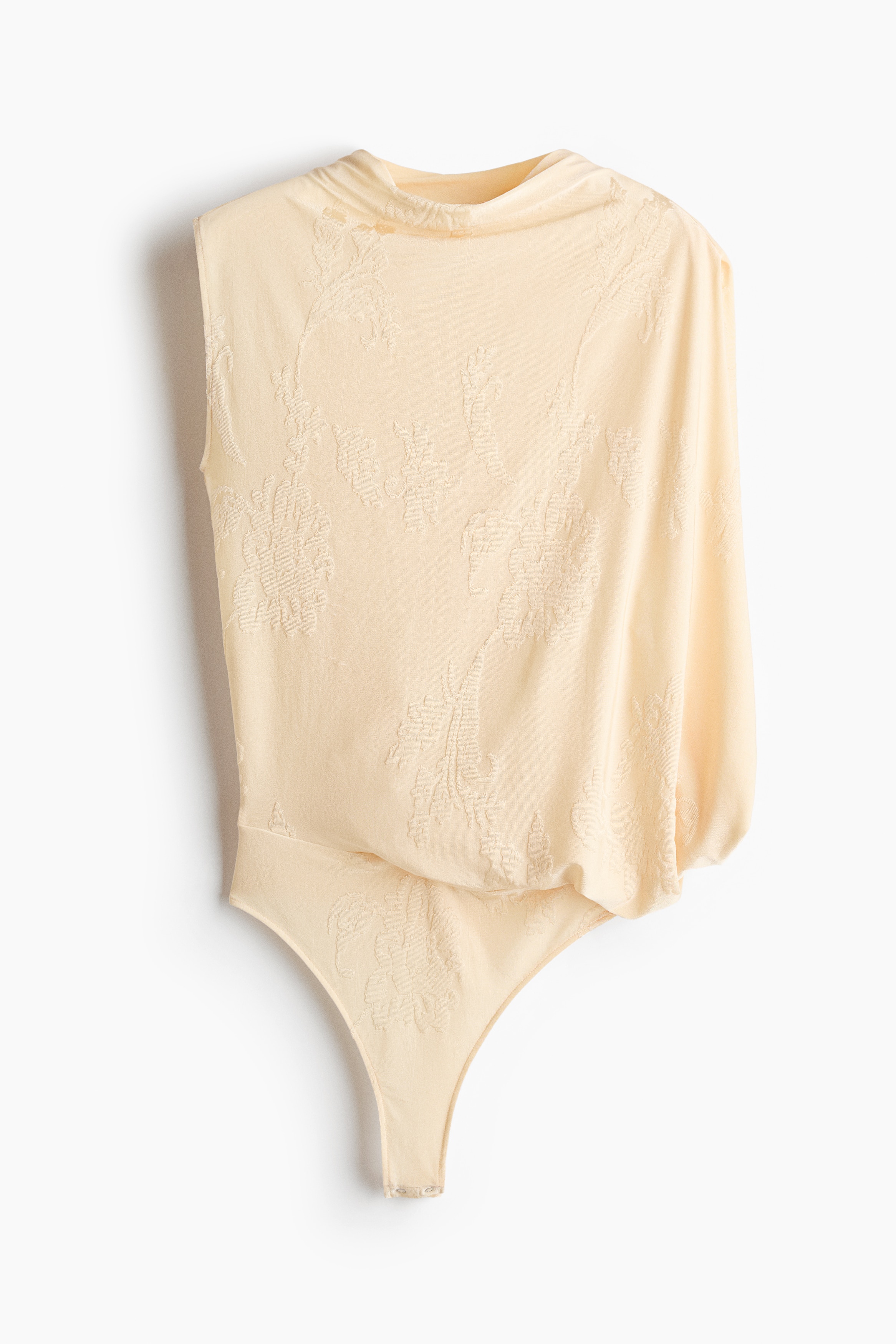 Ein hellgelber Jacquard-Strick-Stringbody mit hohem Rundhalsausschnitt, einem kurzen Ãrmel auf einer Seite und einem drapierten Cape-Ãrmel auf der anderen wird vom Model getragen. Der Body ist in eine locker sitzende, tief sitzende, used-look Denim-Jeans gesteckt, um das hoch geschnittene Hüftdetail des Kleidungsstücks zu zeigen.