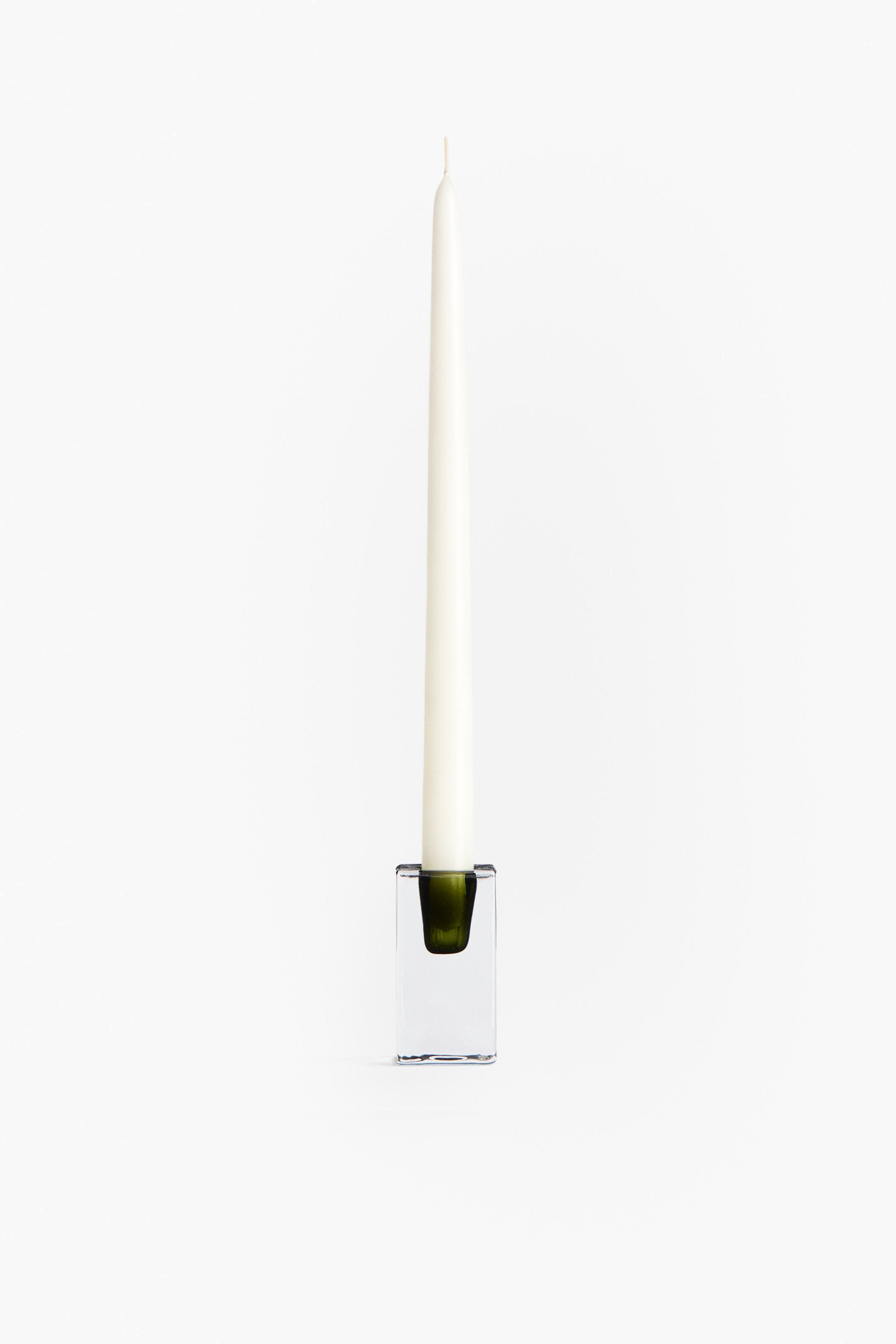 View larger image: A candlestick features a thick, clear rectangular glass base with an olive green accent-colored socket. A white tapered candle stands upright in the socket, facing forward.