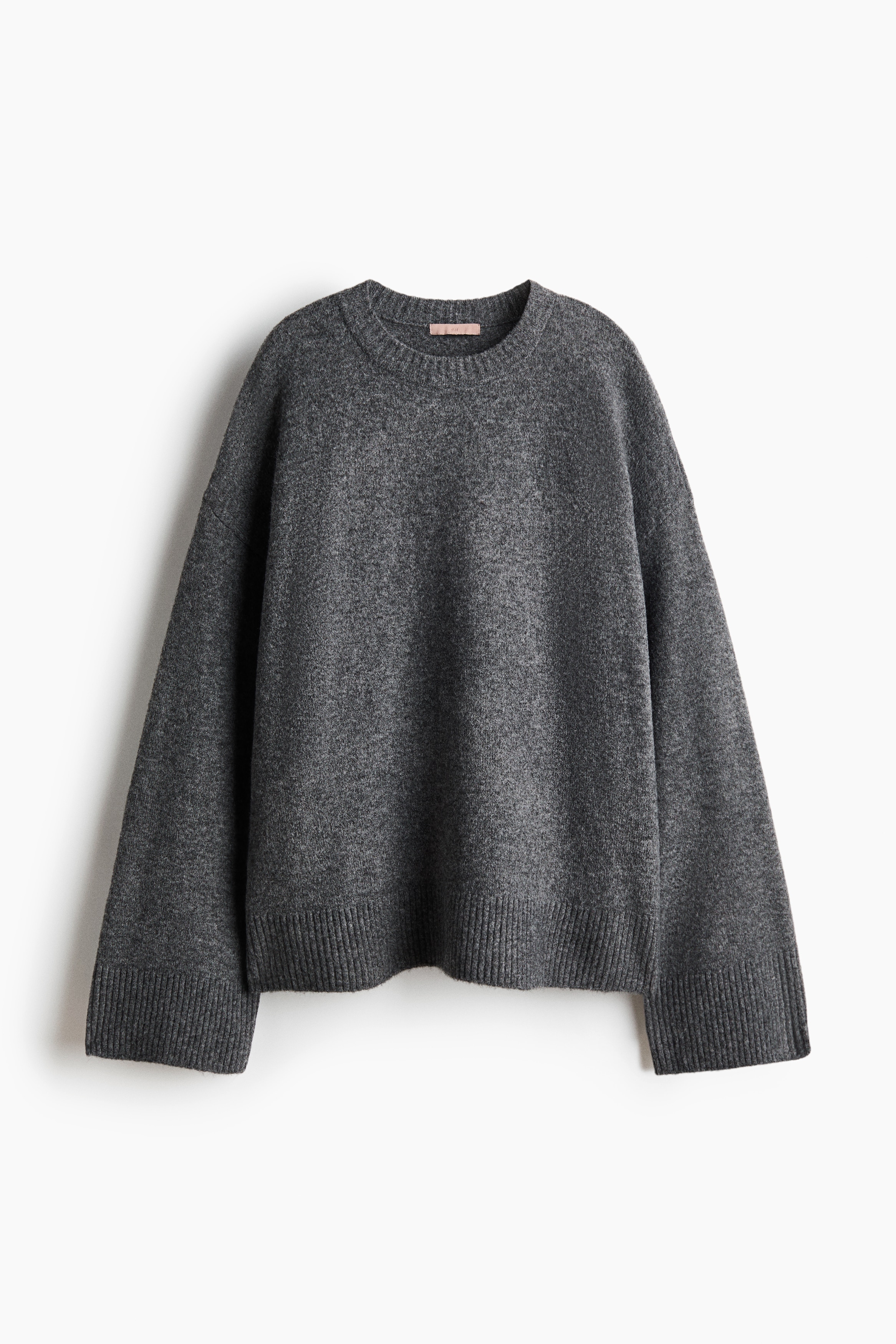 A knitted sweater with a ribbed crew neckline is being worn by the model, who is raising both arms to hold the fabric near their head. This black-and-white close-up highlights the soft, textured finish of the knit.