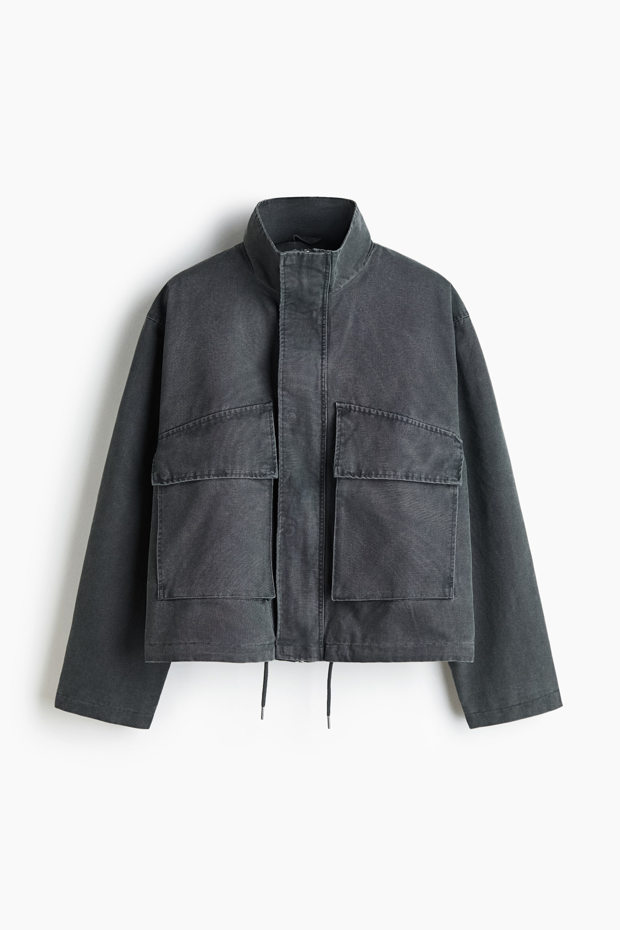 View larger image: A dark grey utility jacket is shown from the front, featuring a high stand-up collar, concealed front closure, and two large front patch pockets with flaps. The jacket has a boxy silhouette with dropped shoulders, a washed fabric finish, and thin drawstrings hanging from the bottom hem.