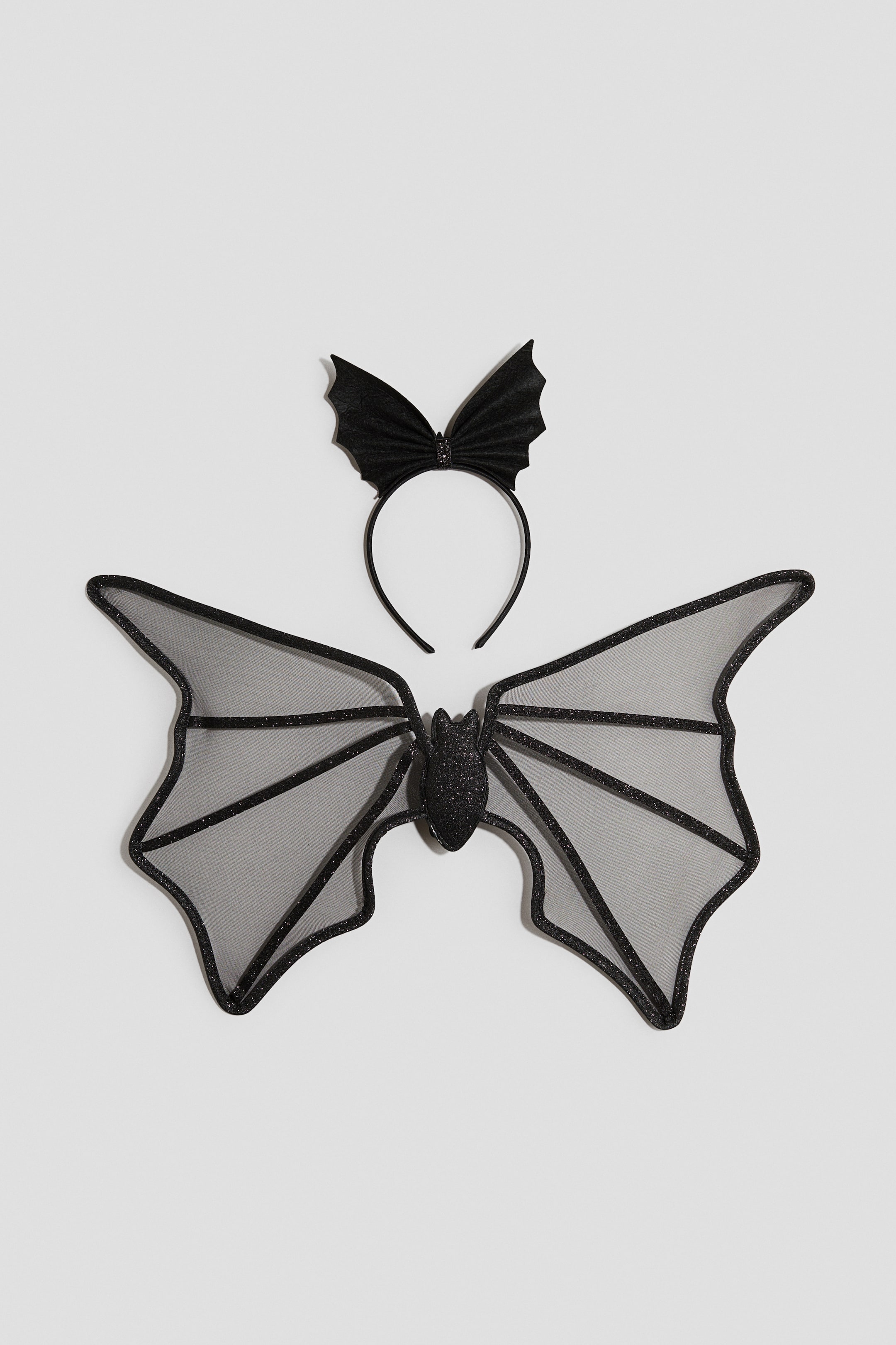 Größeres Bild ansehen: Ein schwarzes Fledermaus-Kostümset wird von vorne gezeigt und besteht aus einem Paar transparenter, grauschwarzer Mesh-Flügel mit glitzernder schwarzer Verstärkung und Einfassung sowie einem passenden schwarzen Haarreif, der mit einer schleifenförmigen Verzierung in Fledermausflügel-Optik geschmückt ist.