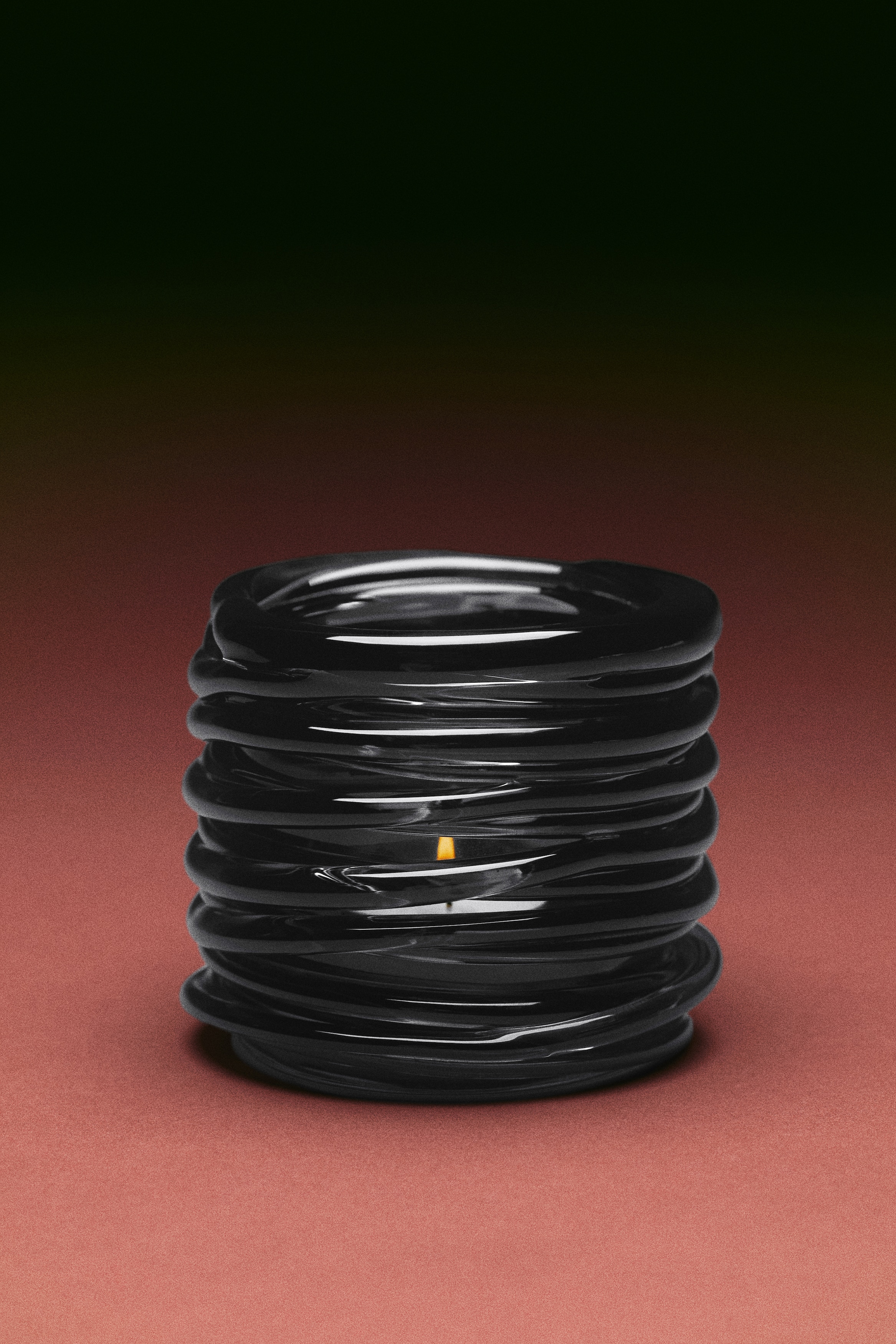 A black glass tealight holder stands elegantly, showcasing a sculptural, coiled design. Its cylindrical shape is crafted from multiple stacked, smooth rings of glass.