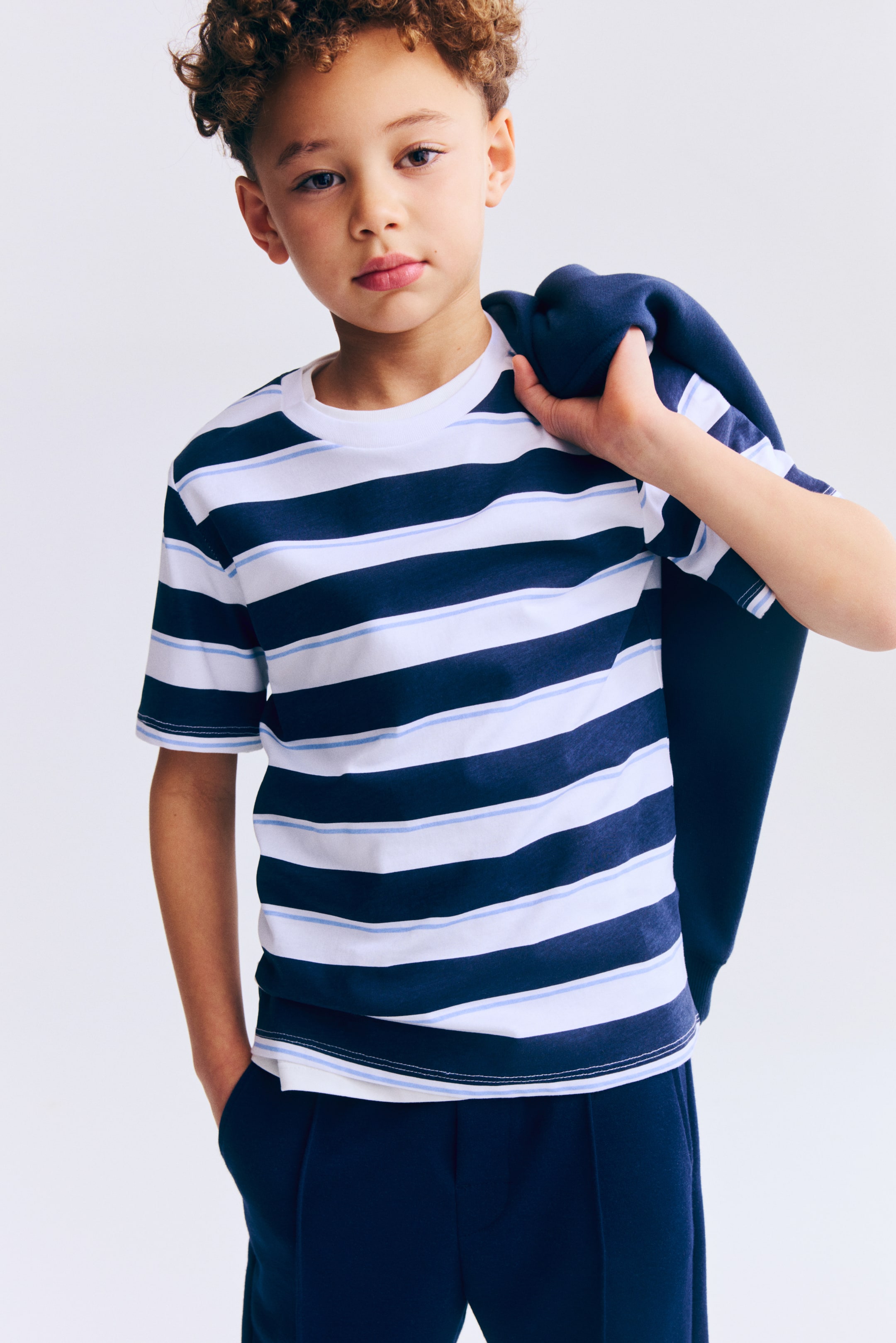 View larger image: A T-shirt features horizontal stripes in white, dark blue and light blue, with stripes of varying widths. It has a crew neck and short sleeves, presented from the front.