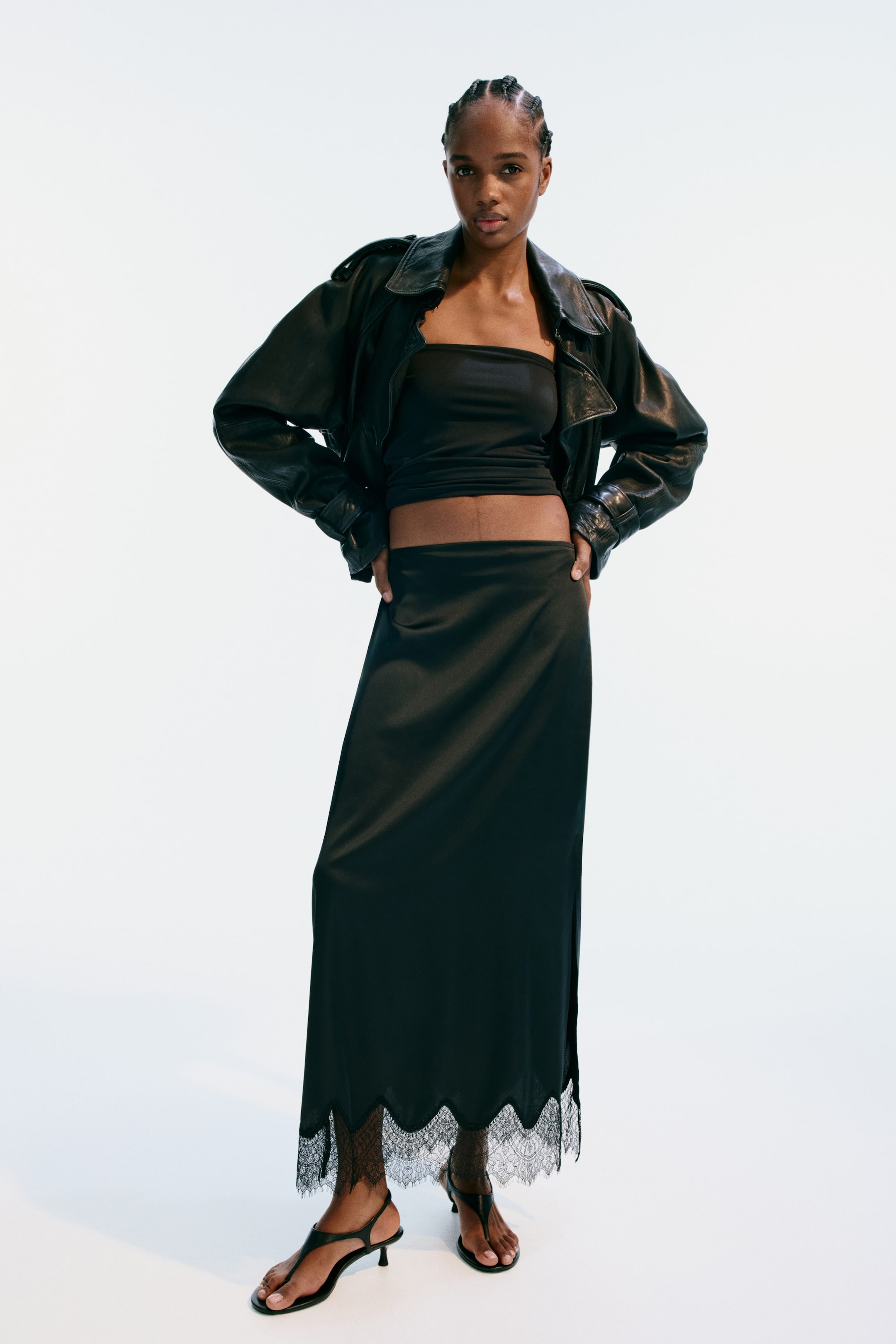 View larger image: A black maxi skirt showcasing a smooth, flowing satin-like fabric. Its high waistline sits flat, with the skirt cascading straight down to the ankles, where a scalloped black lace trim adorns the hem.
