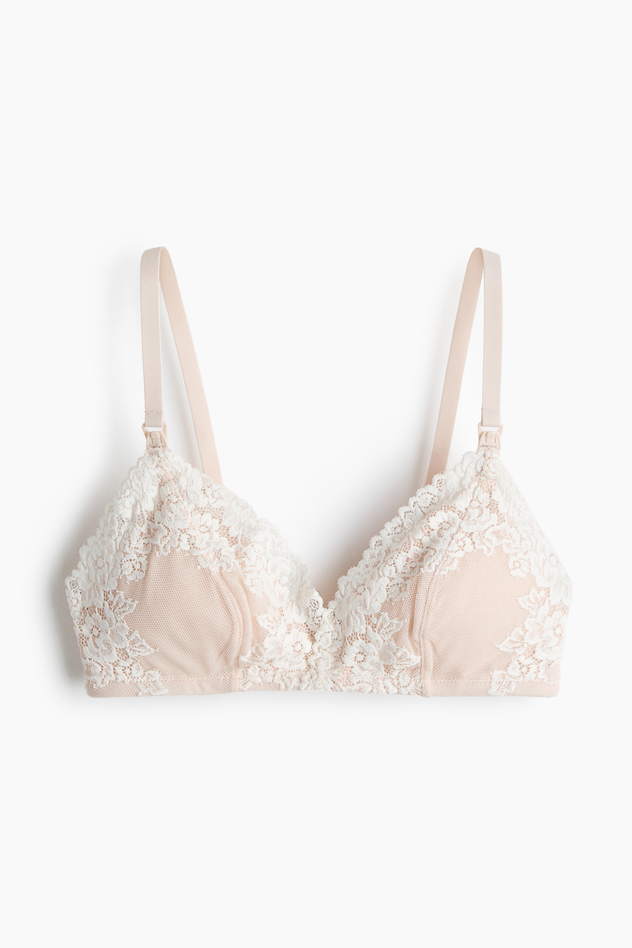 Ingrandisci l'immagine: Un reggiseno frontale presenta una base beige chiaro con sovrapposizione di pizzo floreale bianco sui coppe triangolari. È caratterizzato da sottili spalline beige chiaro regolabili con clip visibili vicino alle coppe.