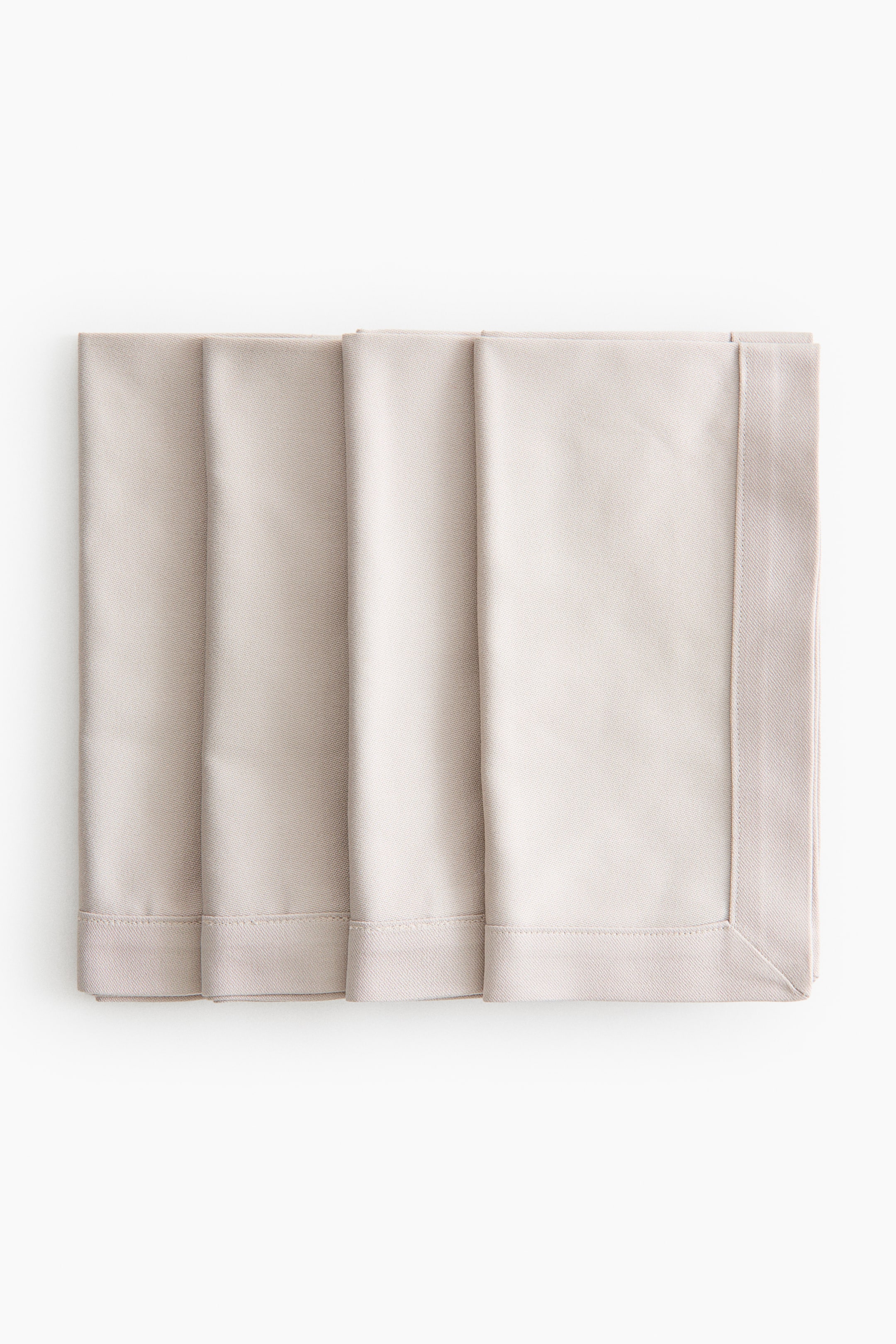 Ver imagen más grande: Cuatro servilletas de color beige claro están dobladas y apiladas con pulcritud, ligeramente superpuestas. Cada servilleta presenta un amplio borde cosido con una trama de sarga visible, enmarcando el tejido central más liso.