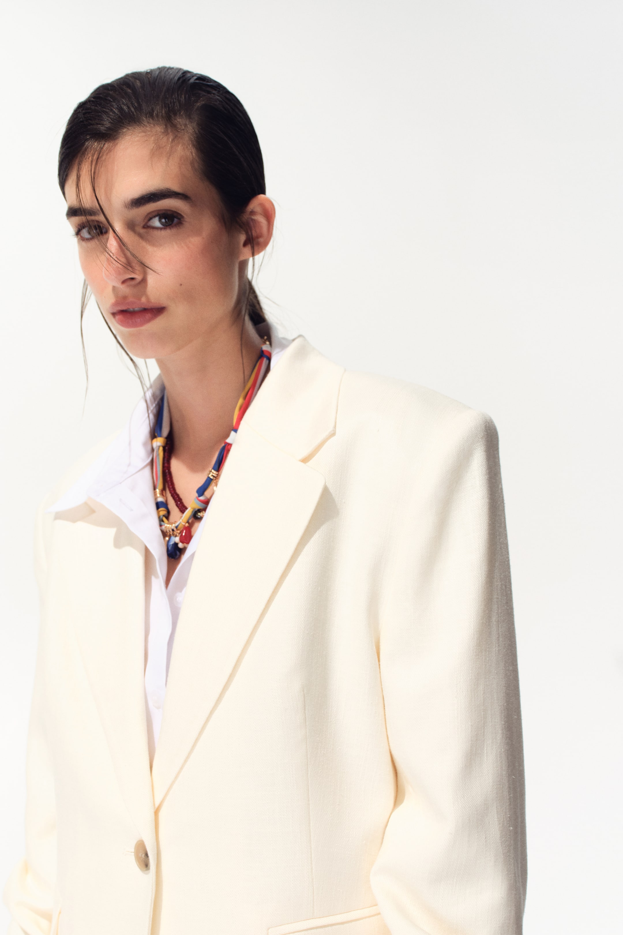 Ampliar la imagen: Un blazer color crema se muestra desde un ángulo frontal derecho, con hombros estructurados y solapas de muesca sobre una camisa blanca con cuello. Presenta un cierre de botón marrón claro y un bolsillo con solapa en el frente.