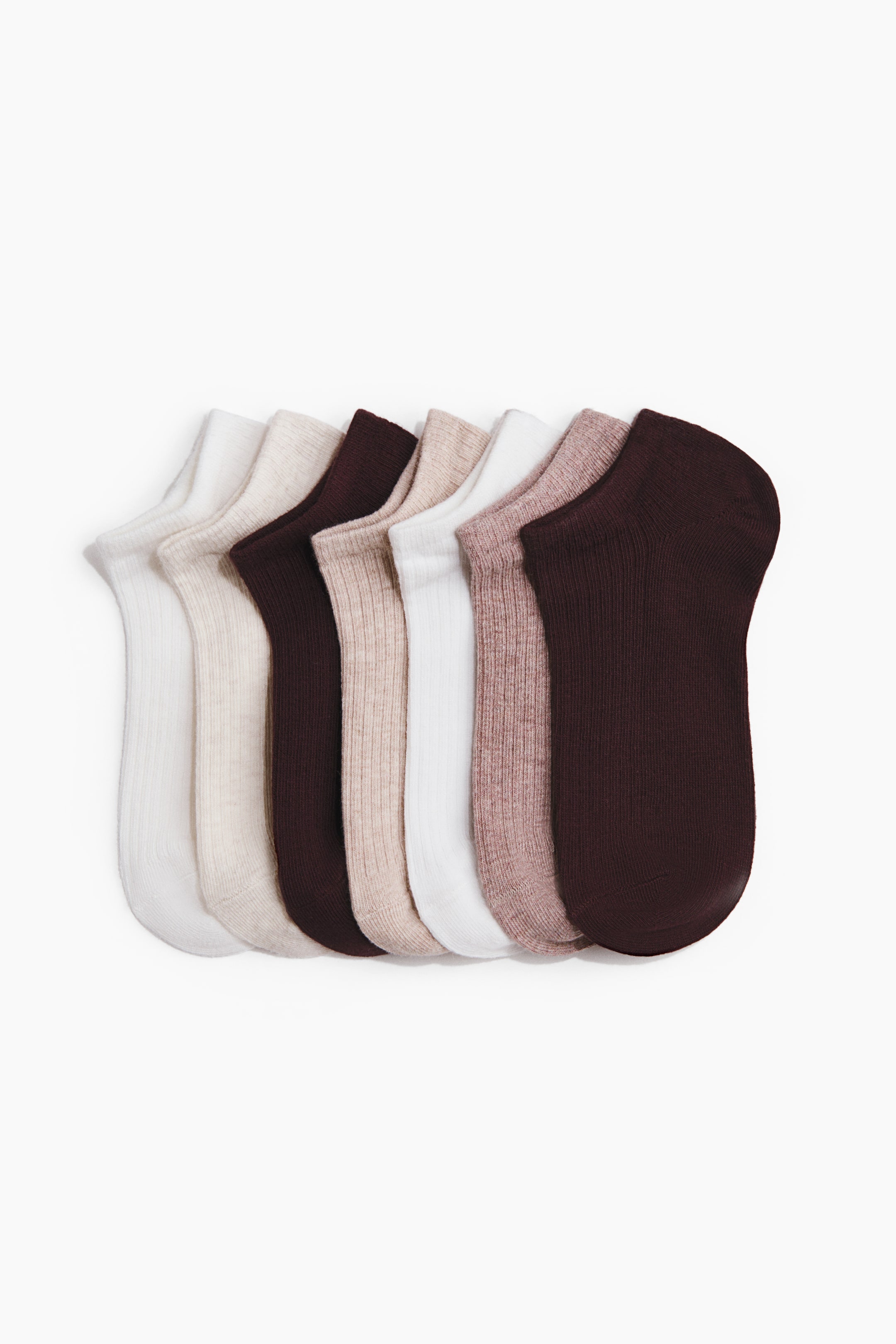 View larger image: Fine-knit trainer socks crafted from a soft cotton blend, featuring elasticated tops, are displayed in an overlapping, fanned-out arrangement. The set includes seven pairs in a variety of neutral tones such as white, cream, light brown, dusty rose, and dark brown. Some socks are detailed with a ribbed texture on their cuffs.