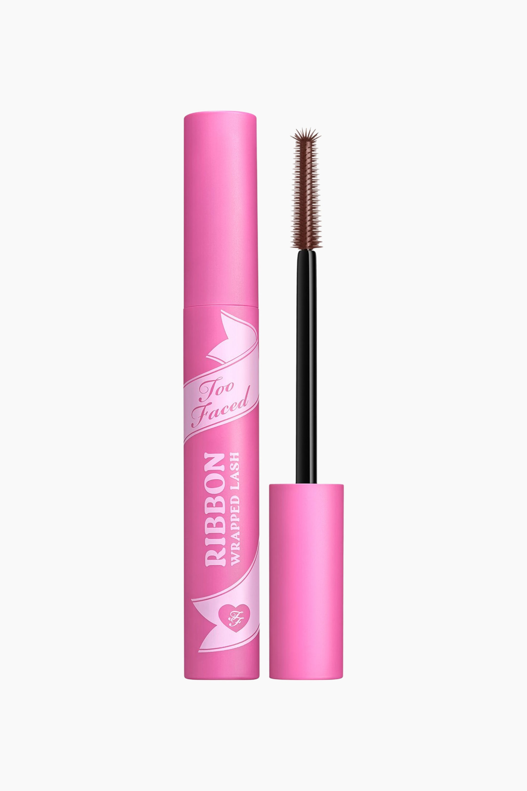 Visa större bild: En rosa mascaratub står upprätt, med ett rosa banddesign och texten "Too Faced Ribbon Wrapped Lash". Dess lösa borste, med ett svart skaft och ett brunt borsthuvud, står upprätt bredvid, medan den matchande rosa korken vilar vid borstens bas.