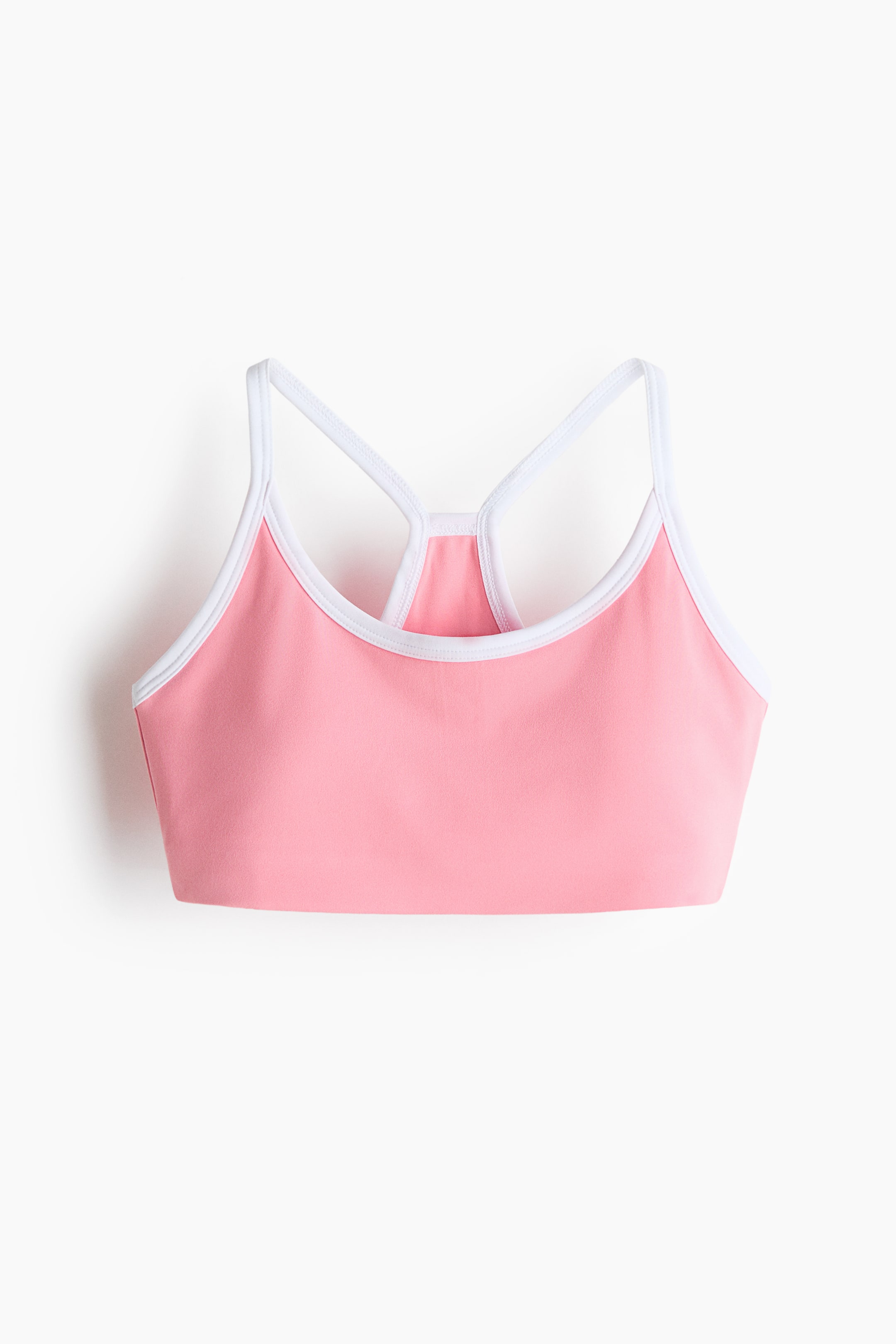 Agrandir l'image: Un soutien-gorge de sport rose avec des bordures blanches le long de son encolure dégagée et de ses emmanchures. Il est conçu avec une configuration de bretelles dos nageur, présenté de face.