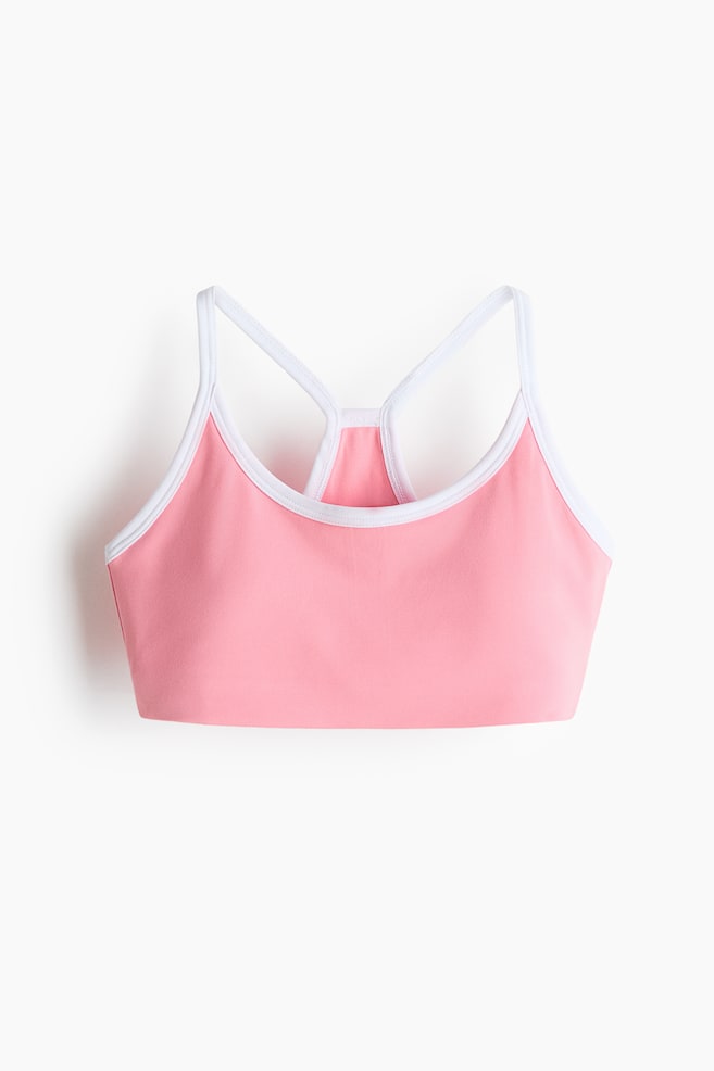 A pink sports bra is featuring white trim along its scoop neckline and armholes. It is designed with a racerback strap configuration, presented from a front-facing angle. - 1
