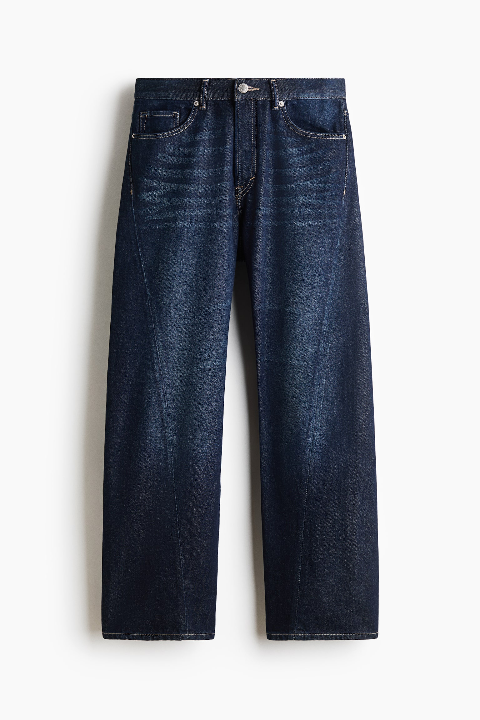 Een paar donkerblauwe, losvallende denim jeans wordt frontaal getoond, met een rechte pijp en een normale taille met knoopsluiting. De jeans heeft een opvallende gedraaide naad die diagonaal over de voorkant van elk been loopt en subtiele vervaging over de bovenbenen.