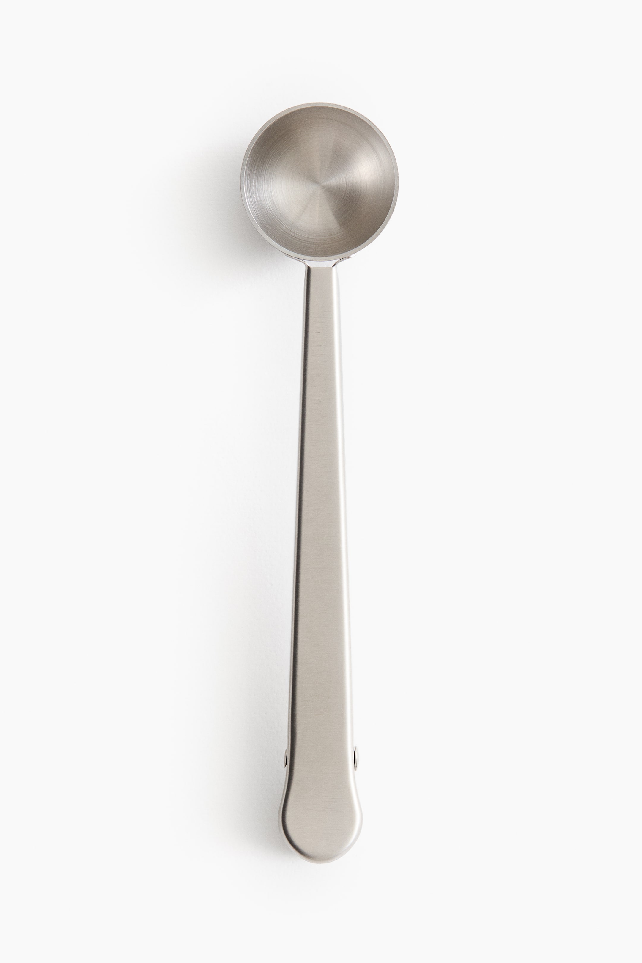 Voir une image plus grande: Une cuillère à mesurer en métal brossé est posée à plat, tournée vers le haut. Elle présente une tête de cuillère ronde et peu profonde avec des cercles concentriques sur la surface intérieure, ainsi qu'un long manche plat qui intègre un mécanisme de pince à sac à son extrémité arrondie.