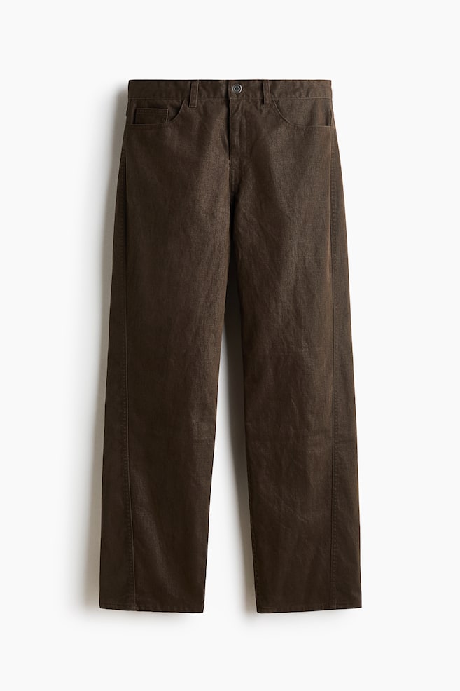 A front view of dark brown five-pocket pants in flocked cotton twill, featuring a relaxed fit with straight legs and forward-facing side seams. The design is showing a waistband with belt loops, a button closure, and a zip fly. - 1