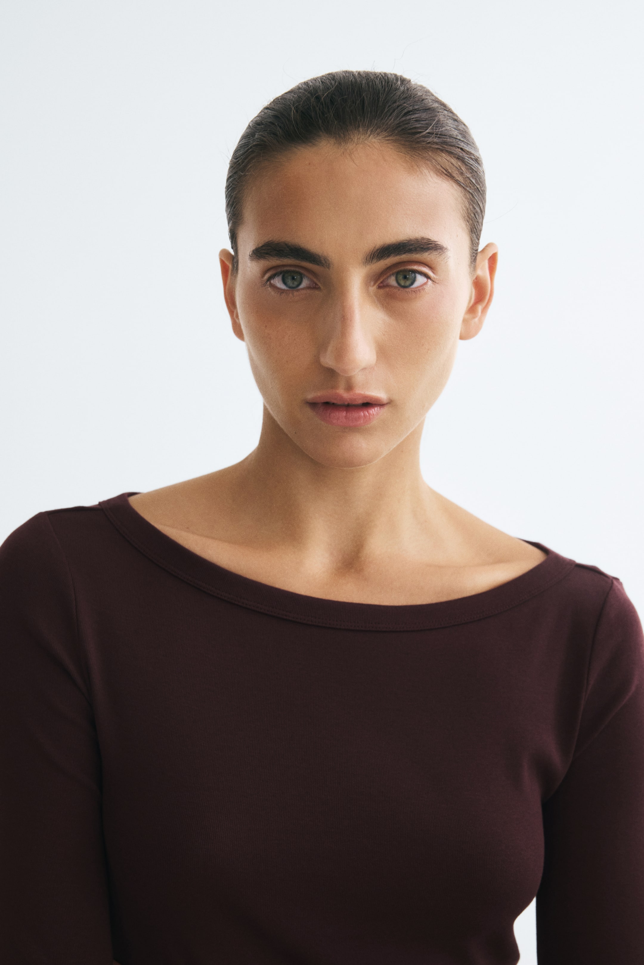 Visa större bild: En mörk burgundy åtsittande topp i fin ribbstickad jersey bärs av modellen. Toppen har en vid båtringning och långa ärmar.
