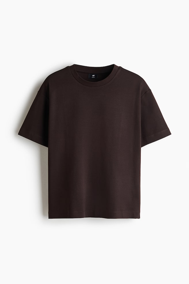 A dark brown cotton interlock jersey t-shirt is facing front, displaying a boxy, loose-fit silhouette. The t-shirt features a round, rib-trimmed neckline, dropped shoulders, wide short sleeves, and a straight-cut hem. - 1