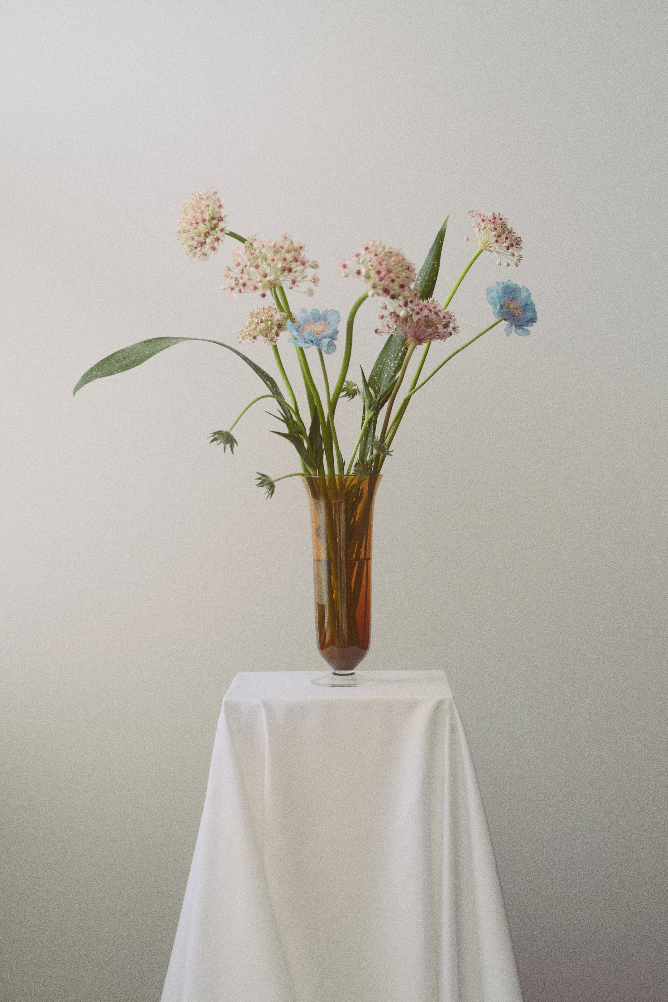 Voir une image plus grande: Le vase haut sur pied est fabriqué en verre teinté ambre, présentant un corps élancé qui s'évase délicatement vers son ouverture et accueillant un bouquet de fleurs.
