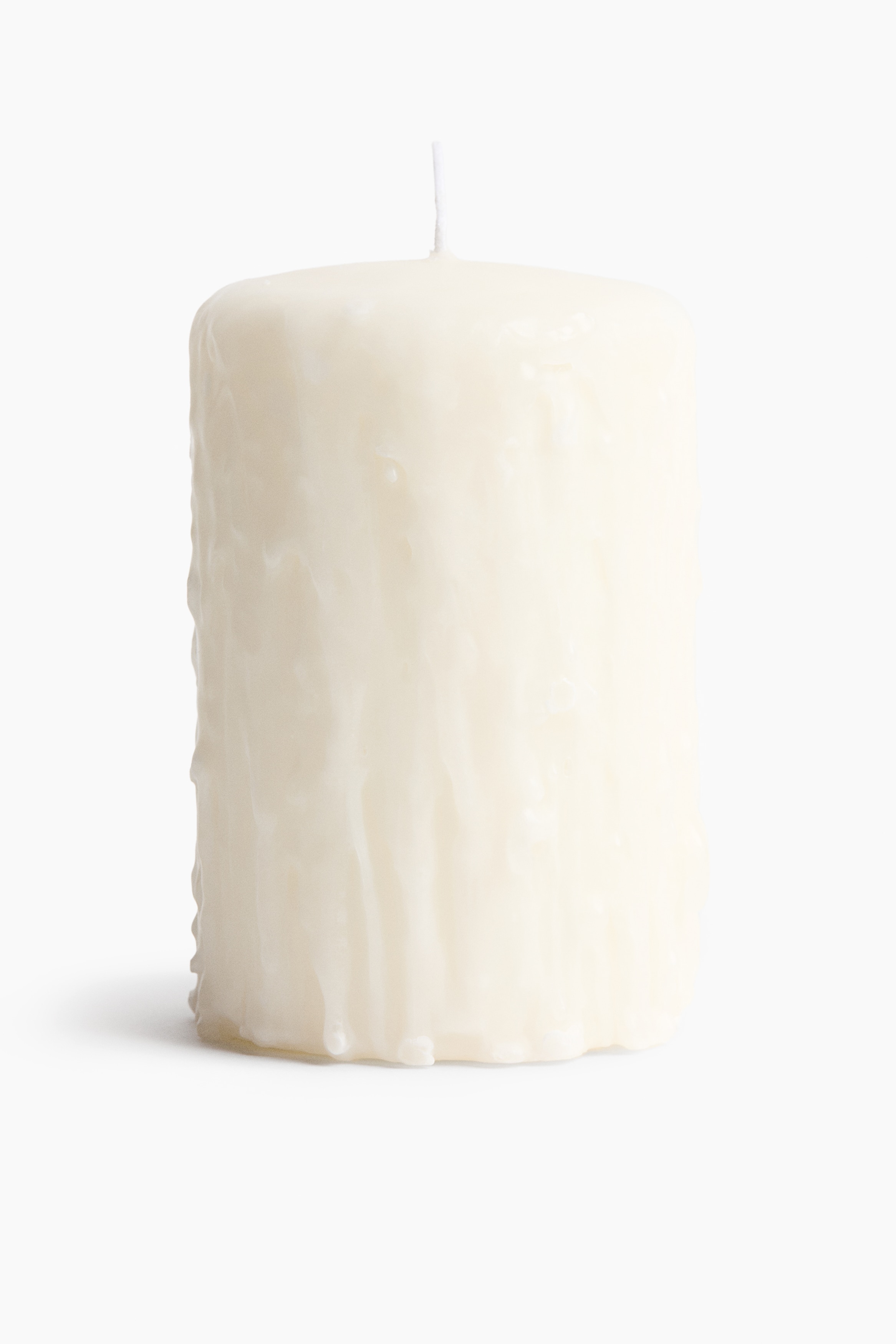 Une grande bougie pilier blanc cassÃ© au design texturÃ© rappelant de la cire qui dÃ©gouline brÃ»le sur un plateau mÃ©tallique, vue de face. La bougie prÃ©sente des gouttes verticales semblables Ã  de la cire le long de ses cÃ´tÃ©s et est allumÃ©e avec une petite flamme Ã  la mÃ¨che, tandis qu'une allumette brÃ»lÃ©e repose sur le plateau Ã  cÃ´tÃ©.