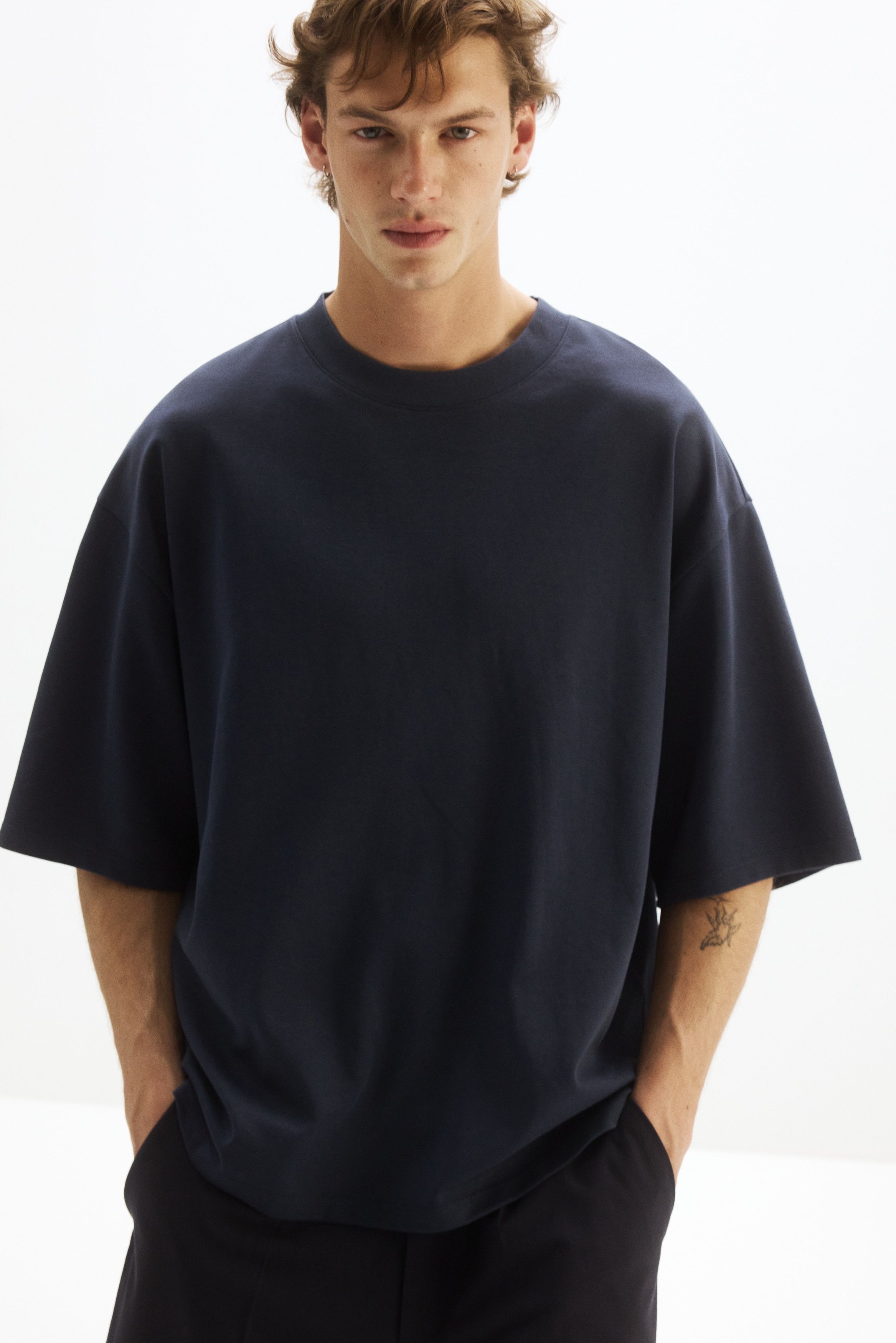 A dark blue t-shirt is presenting from the front, and it is featuring a crew neck and short, wide sleeves. It is having a relaxed, boxy fit with a straight hem, and a small black label is appearing on the inside back neckline.