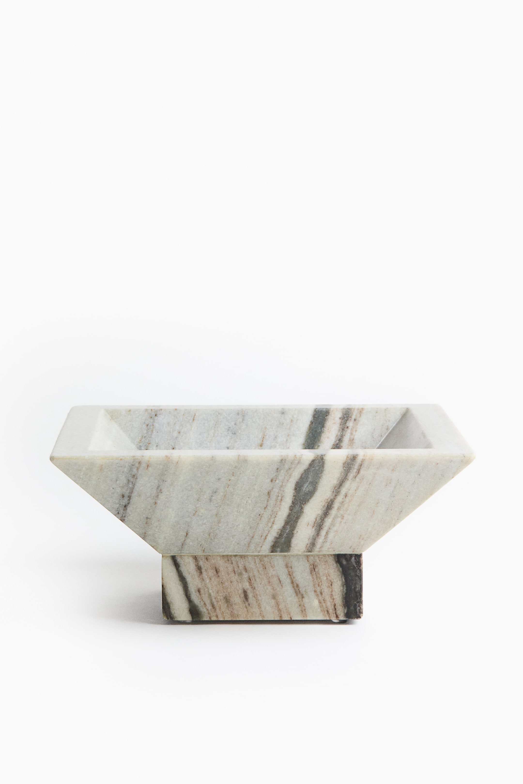 View larger image: A square marble pedestal bowl, shown from the front, rests on a smaller square base and features a flared, inverted-trapezoidal shape with a shallow basin. The natural stone displays prominent brown, beige, and grey veining across its smooth surface.