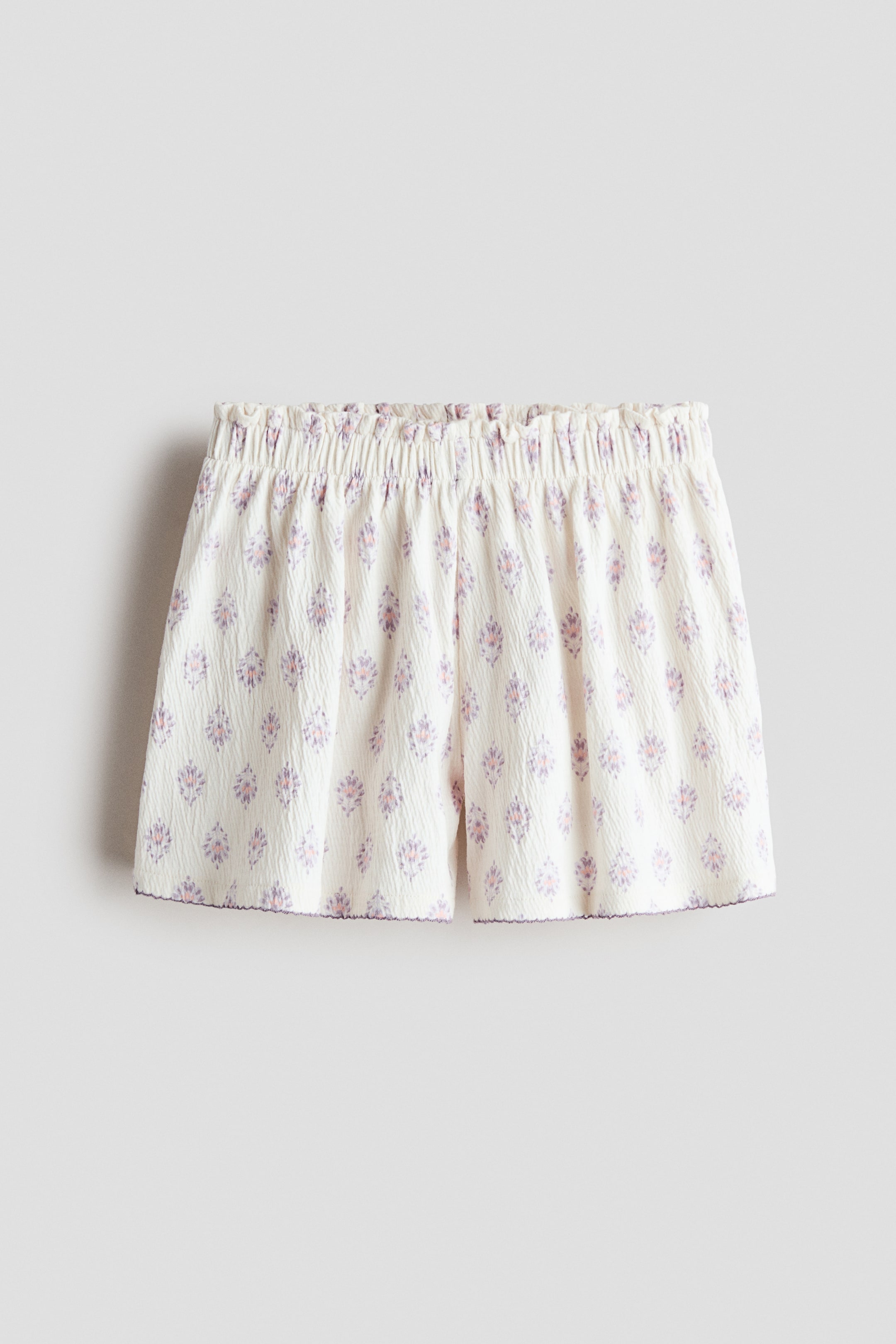 Grotere afbeelding bekijken: Shorts met een gestructureerde katoenen jersey met een all-over print van kleine paarse en roze motieven, een elastische paperbag taille en picot-afgewerkte zomen.