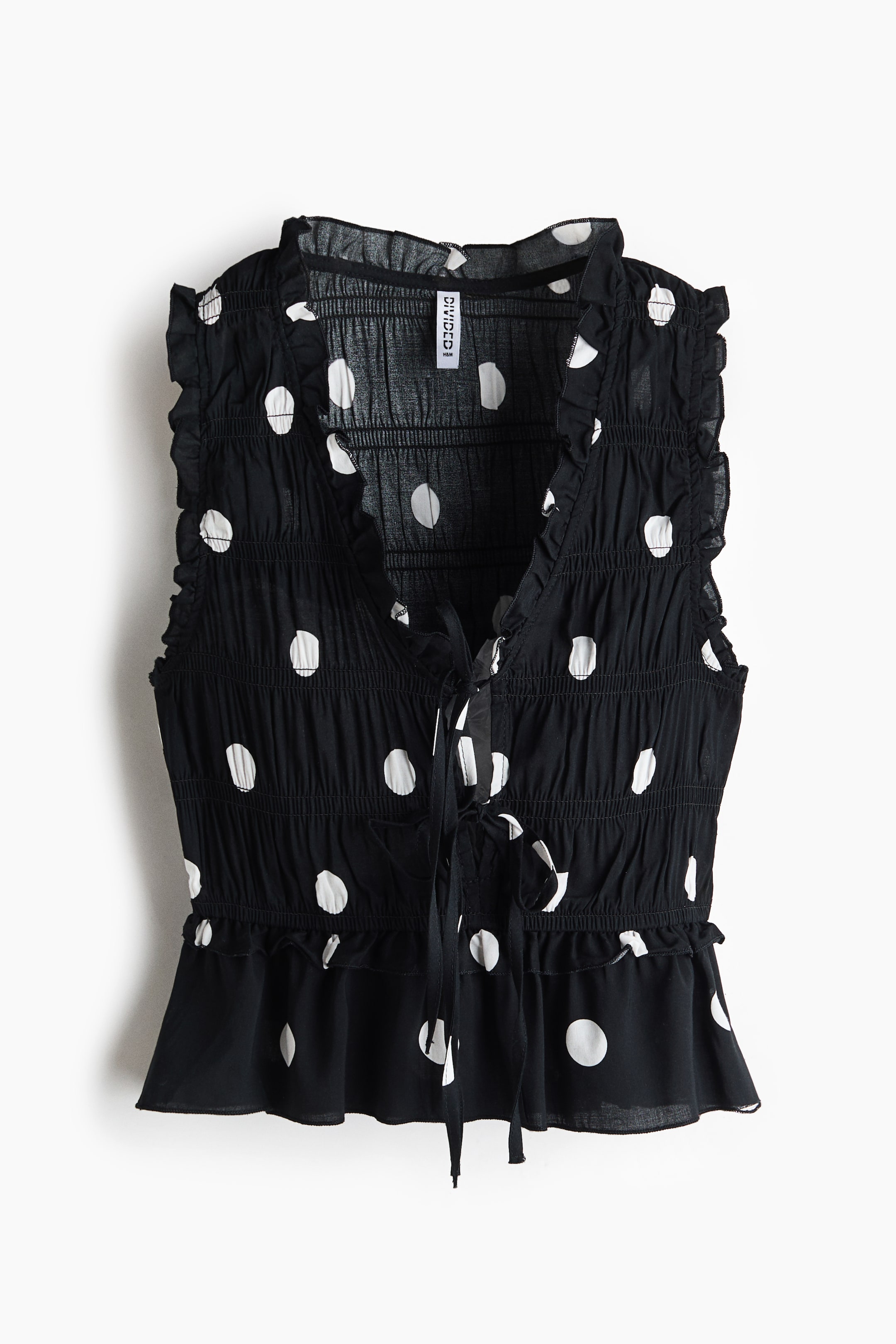 View larger image: A black sleeveless top is displayed in front, featuring white polka dots. It highlights a shirred bodice, a tie-front V-neckline with ruffled trim, ruffled armholes, and a ruffled peplum hem.