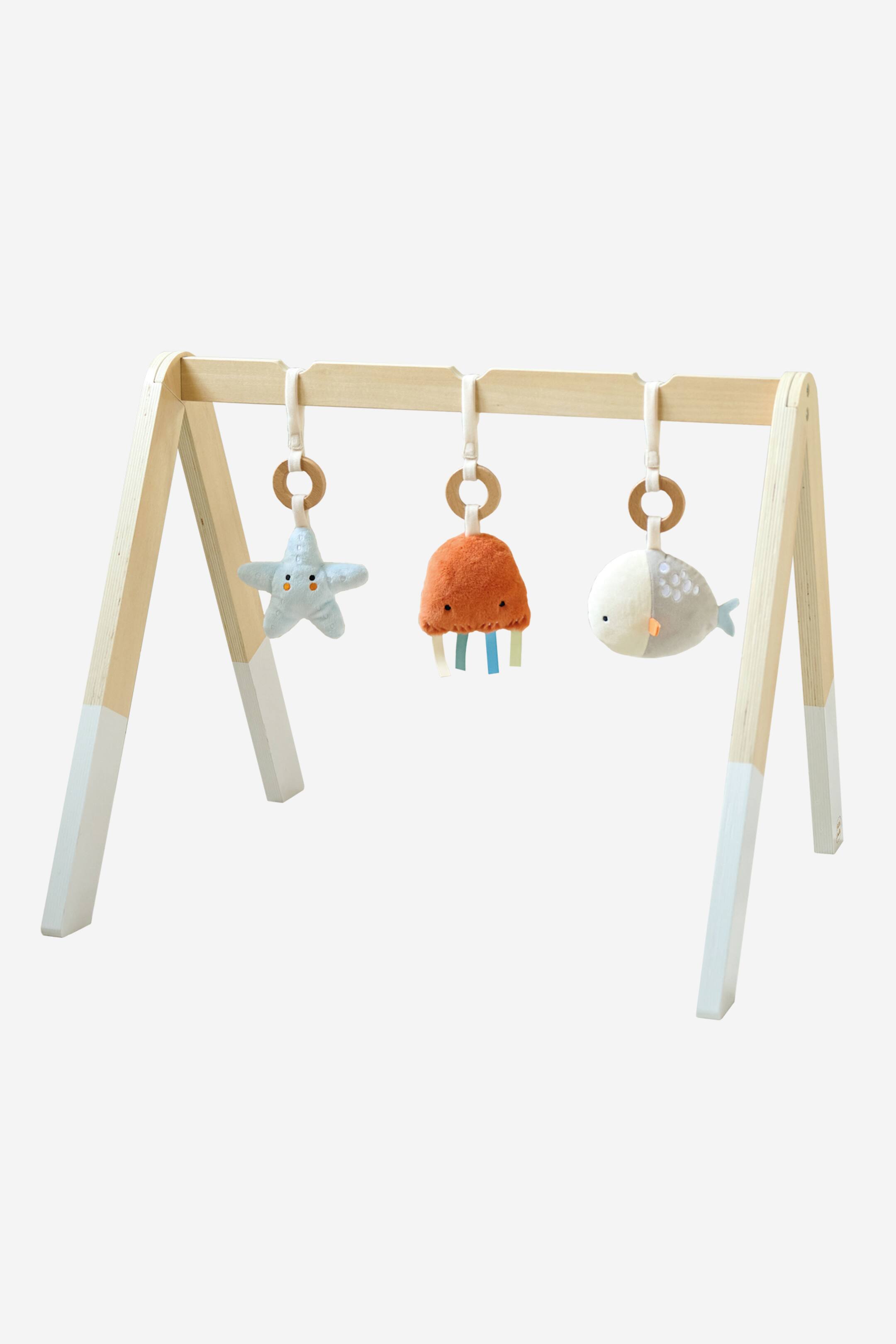 Grotere afbeelding bekijken: Een baby speelgym bevat een licht houten frame met A-frame poten, waarvan de onderste delen in een lichtblauw-grijs zijn geschilderd. Drie zachte speeltjes hangen aan de horizontale balk: een lichtblauwe zeester, een oranje kwal met kleurrijke linttentakels, en een grijs-witte walvis, allemaal naar voren gericht.