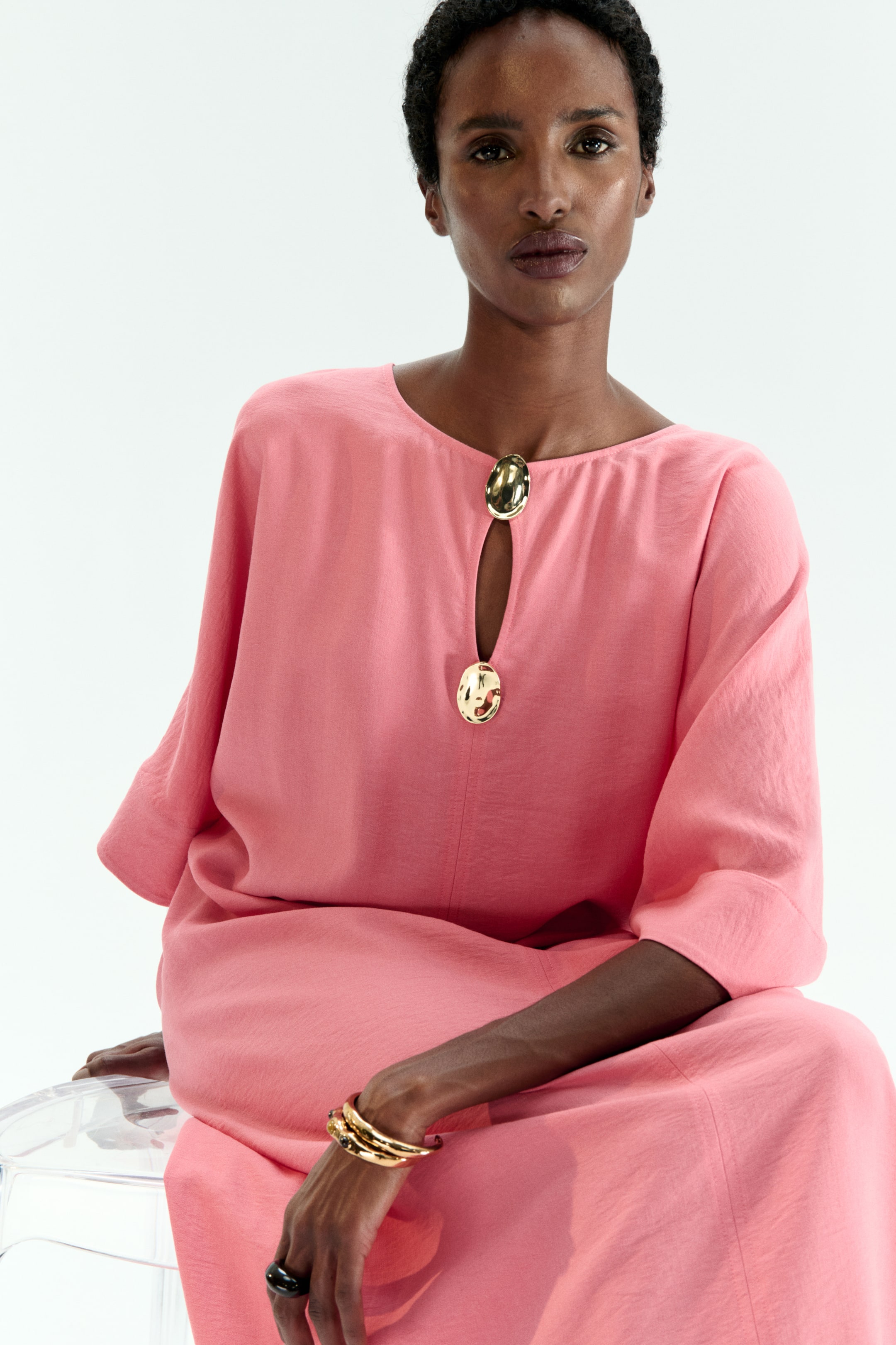 View larger image: A coral dress in a textured fabric is facing forward, featuring a round neckline with a keyhole. Two large, oval, hammered gold-toned buttons are placed above and below the keyhole, and it features wide, three-quarter length sleeves.
