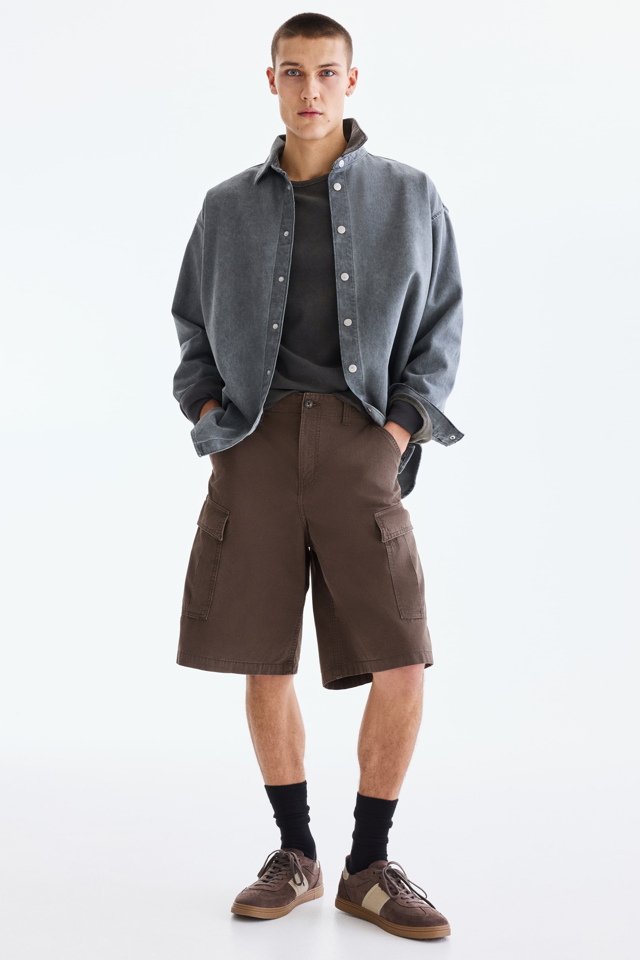 View larger image: Dark brown cargo shorts feature a relaxed fit, extending just above the knees. Designed with side cargo pockets on both thighs and front slash pockets, they include a visible button and zipper closure at the waist.