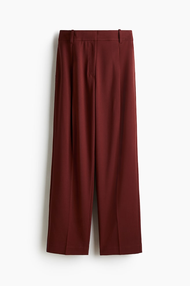 The deep red wide-leg trousers are presenting a flat front, featuring a single front pleat on each leg that extends into a sharp vertical crease. The waistband is showing belt loops. - 1