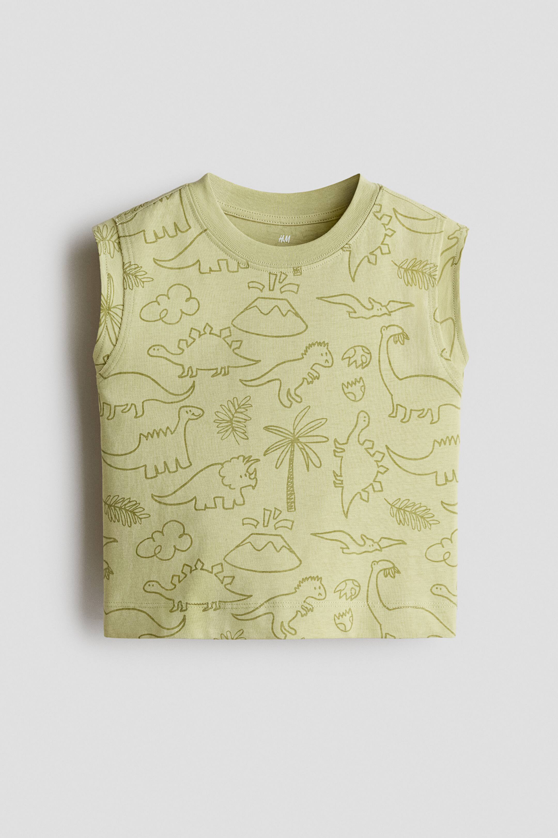 View larger image: A light green sleeveless top is shown from the front, featuring an all-over print of olive-green, line-drawn dinosaurs, volcanoes, and palm trees. The top has a ribbed crew neck and matching ribbed armhole trims.