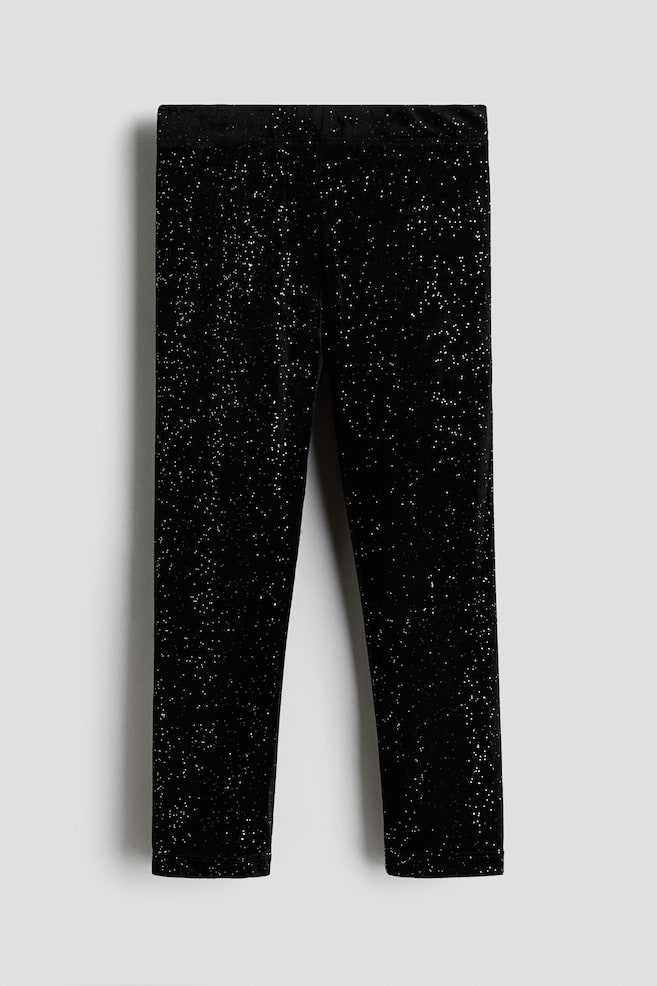 Black velvet leggings are shown from the front, featuring a slim-fit design covered in a speckled silver glitter pattern. The leggings feature a flat elastic waistband and full-length legs. - 1