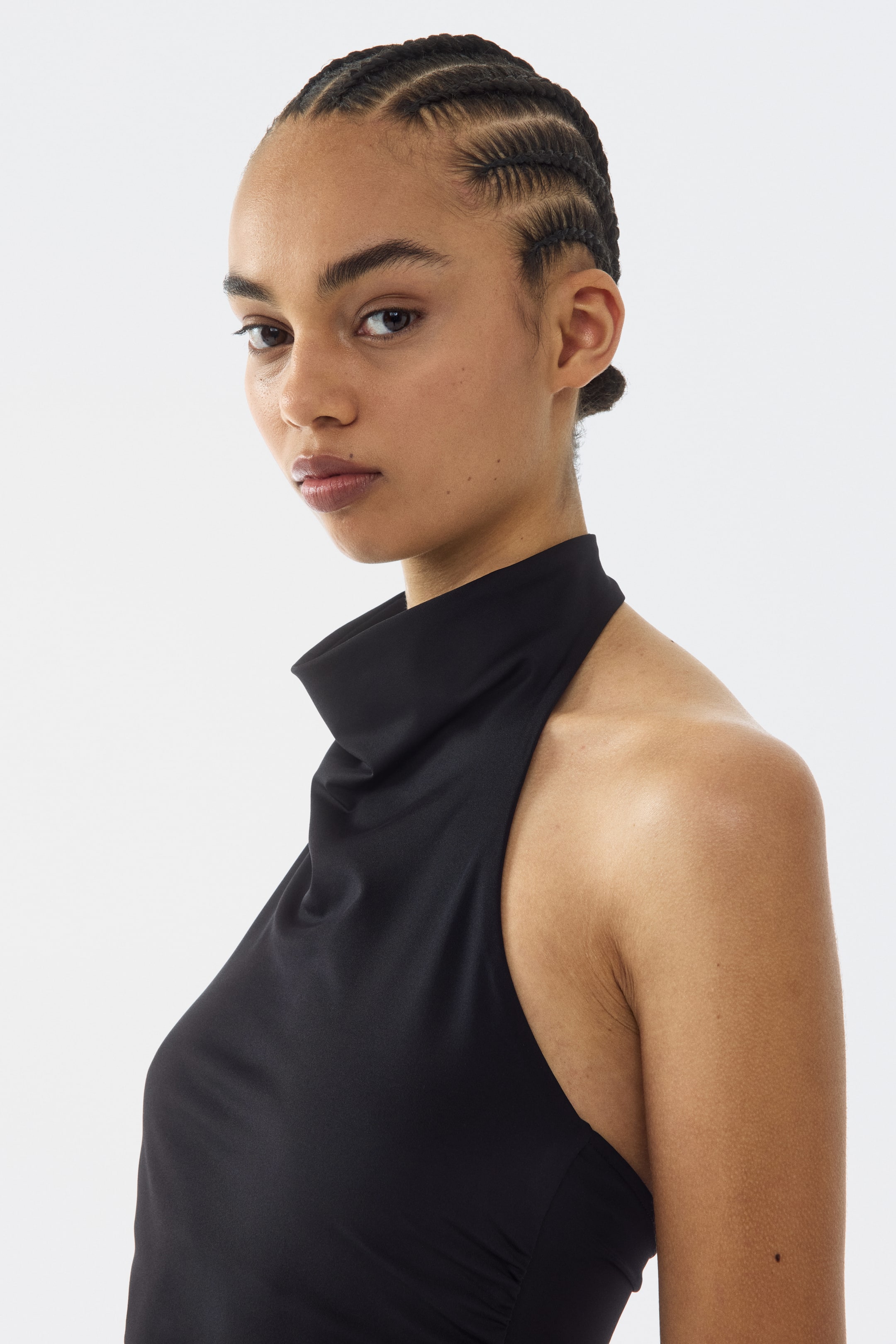 View larger image: A black sleeveless top featuring a high draped neckline, with a smooth finish and a cut-in armhole, displaying subtle gathering along the side.