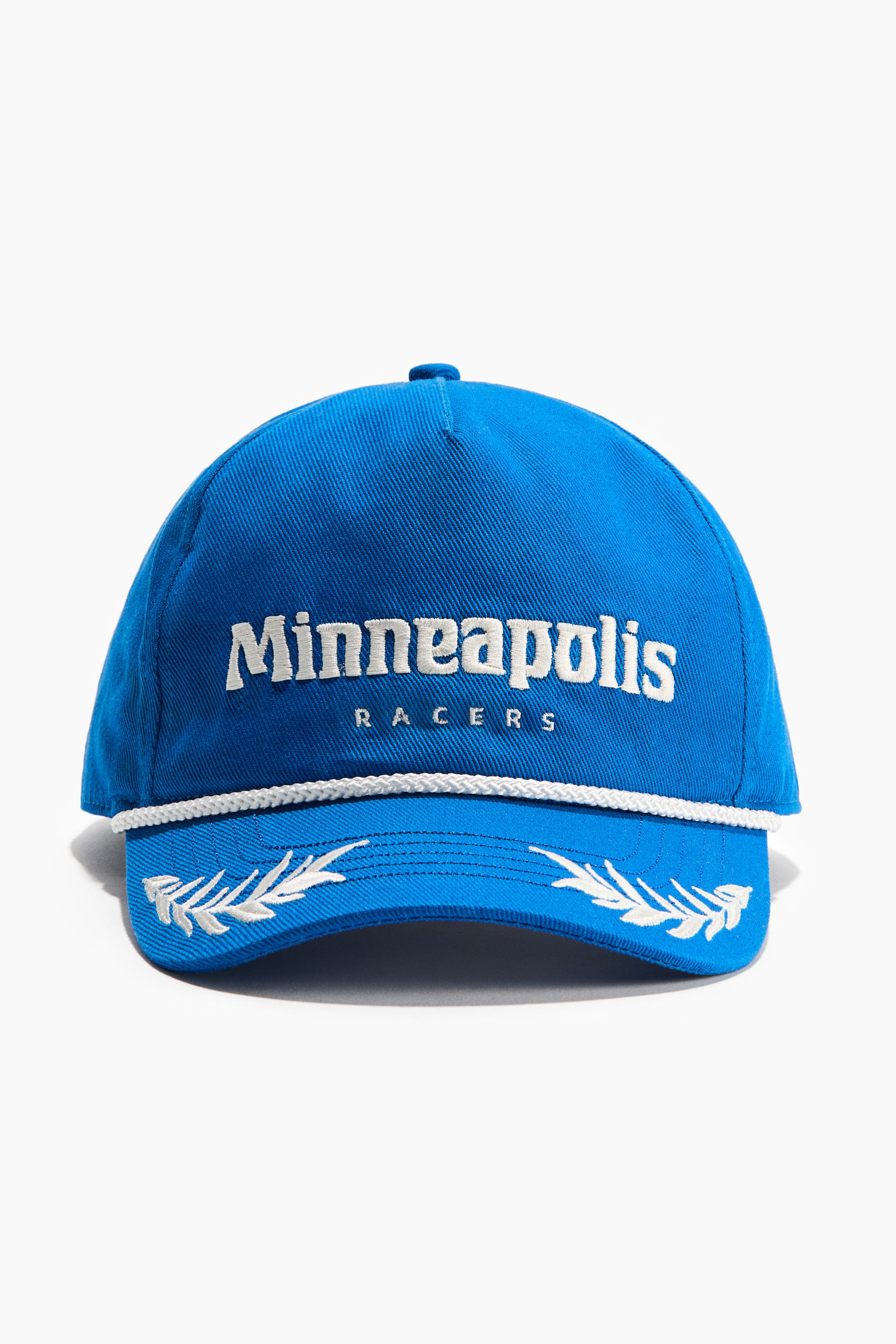 View larger image: A vibrant blue cotton twill cap is showcased front-facing, with 'Minneapolis Racers' embroidered in white on its front panel. A white braided rope runs along the base of the crown, while white embroidered laurel motifs adorn the brim.