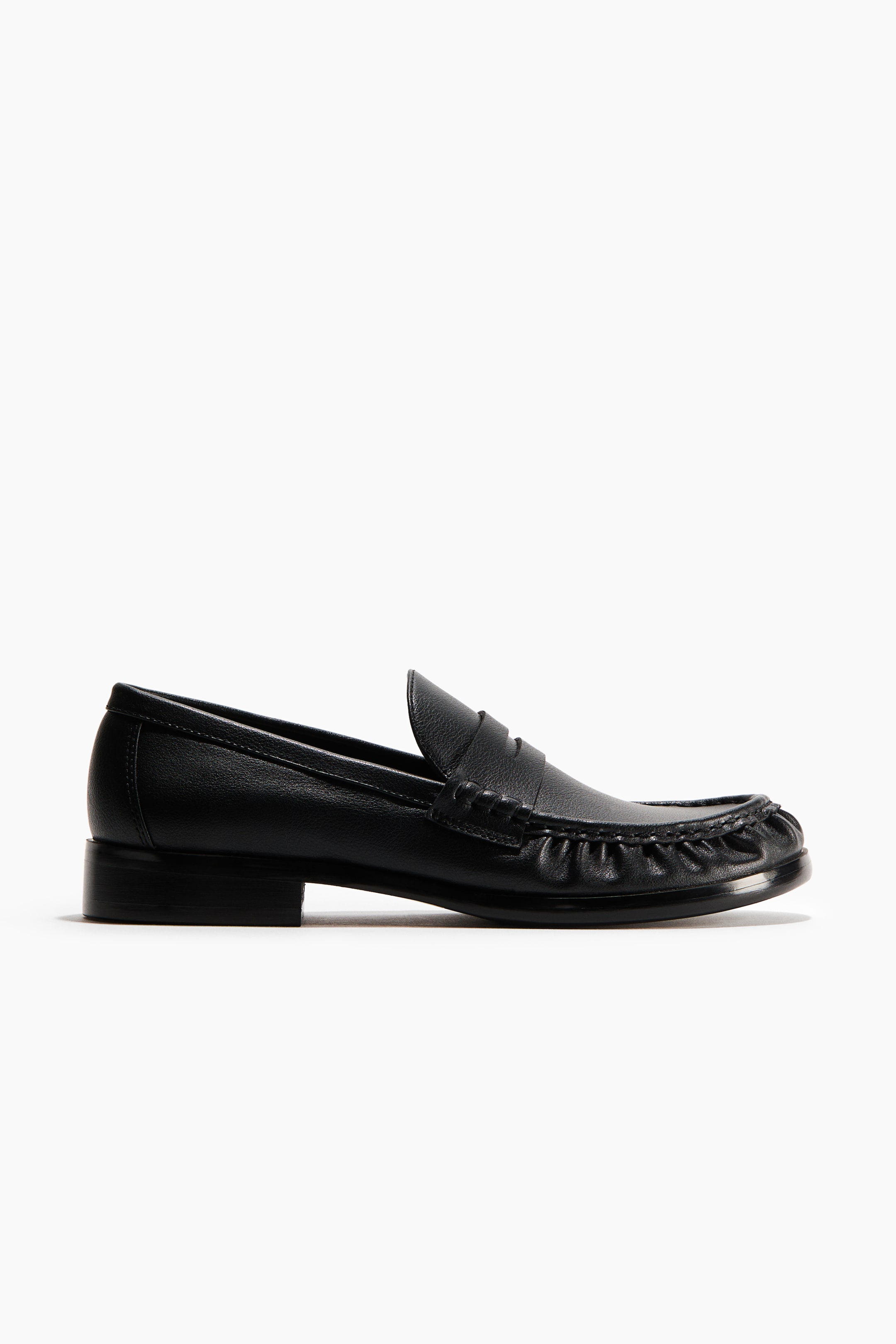 View larger image: A black leather loafer is facing right, featuring a penny strap across the vamp and ruched moccasin-style stitching around the toe box, resting on a low block heel.