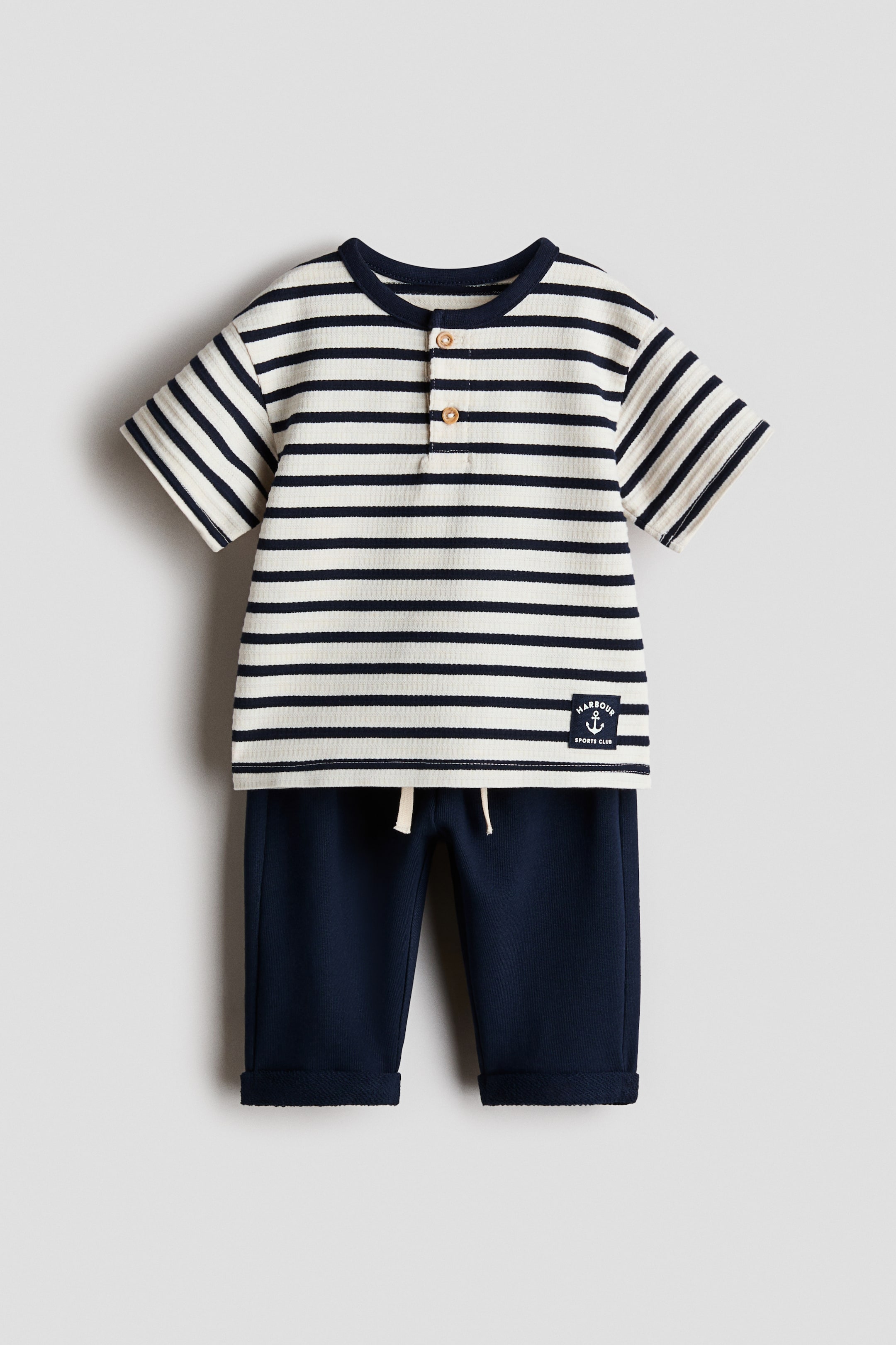 View larger image: A two-piece baby outfit is displaying from the front, featuring a short-sleeved henley top and coordinating pants. 