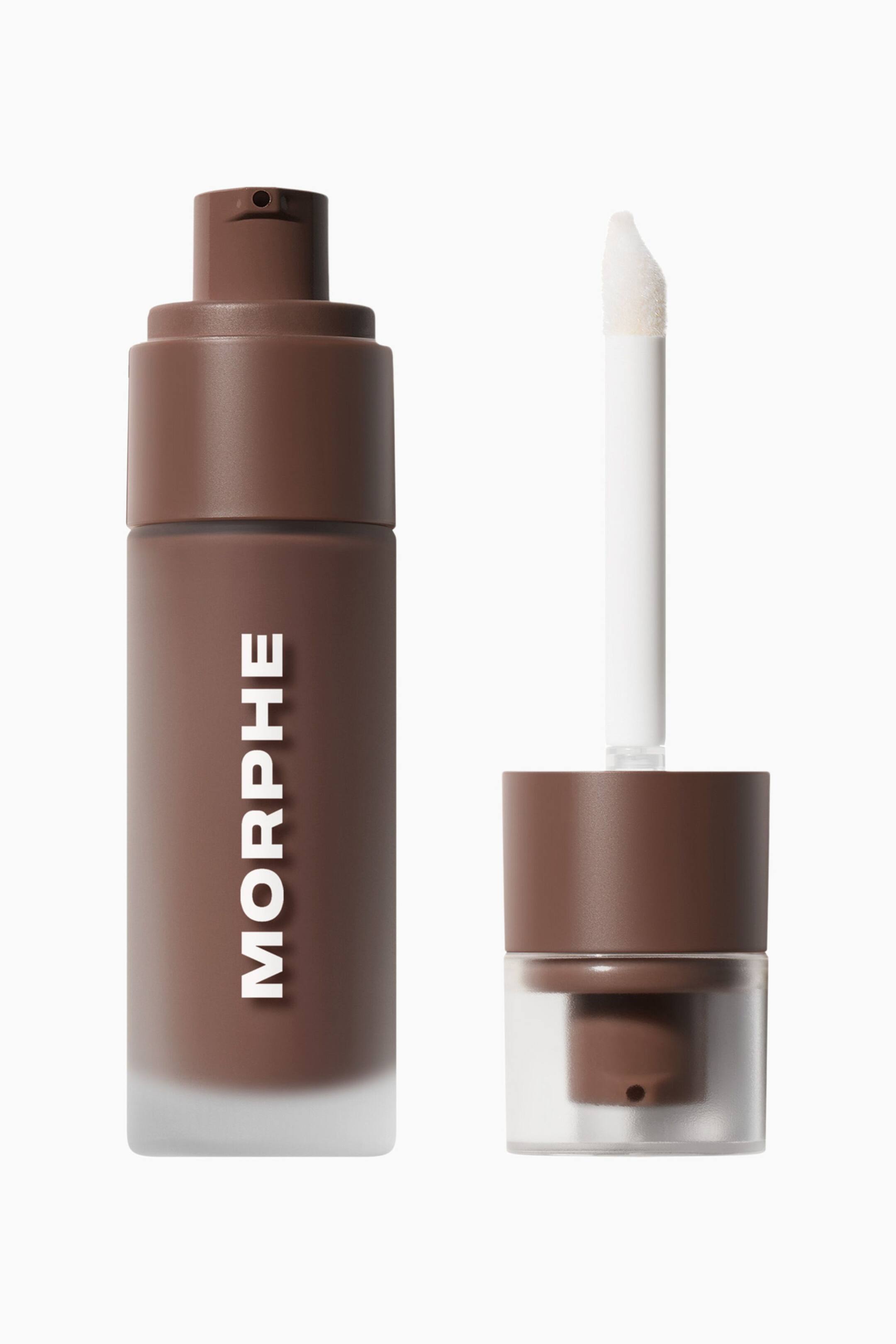 Vis større bilde: Morphe Complexion Boost Peptide Bronzing Serum står oppreist og har en sylindrisk, frostet glassflaske fylt med brun væske, samt en brun pumpe-dispenser med merkenavnet «MORPHE» trykt vertikalt i hvitt. Ved siden av flasken ligger den avtakbare hetten oppå det gjennomsiktige beskyttelsesdekselet, med en hvit stav og en vinklet doe-foot-applikator som strekker seg oppover.