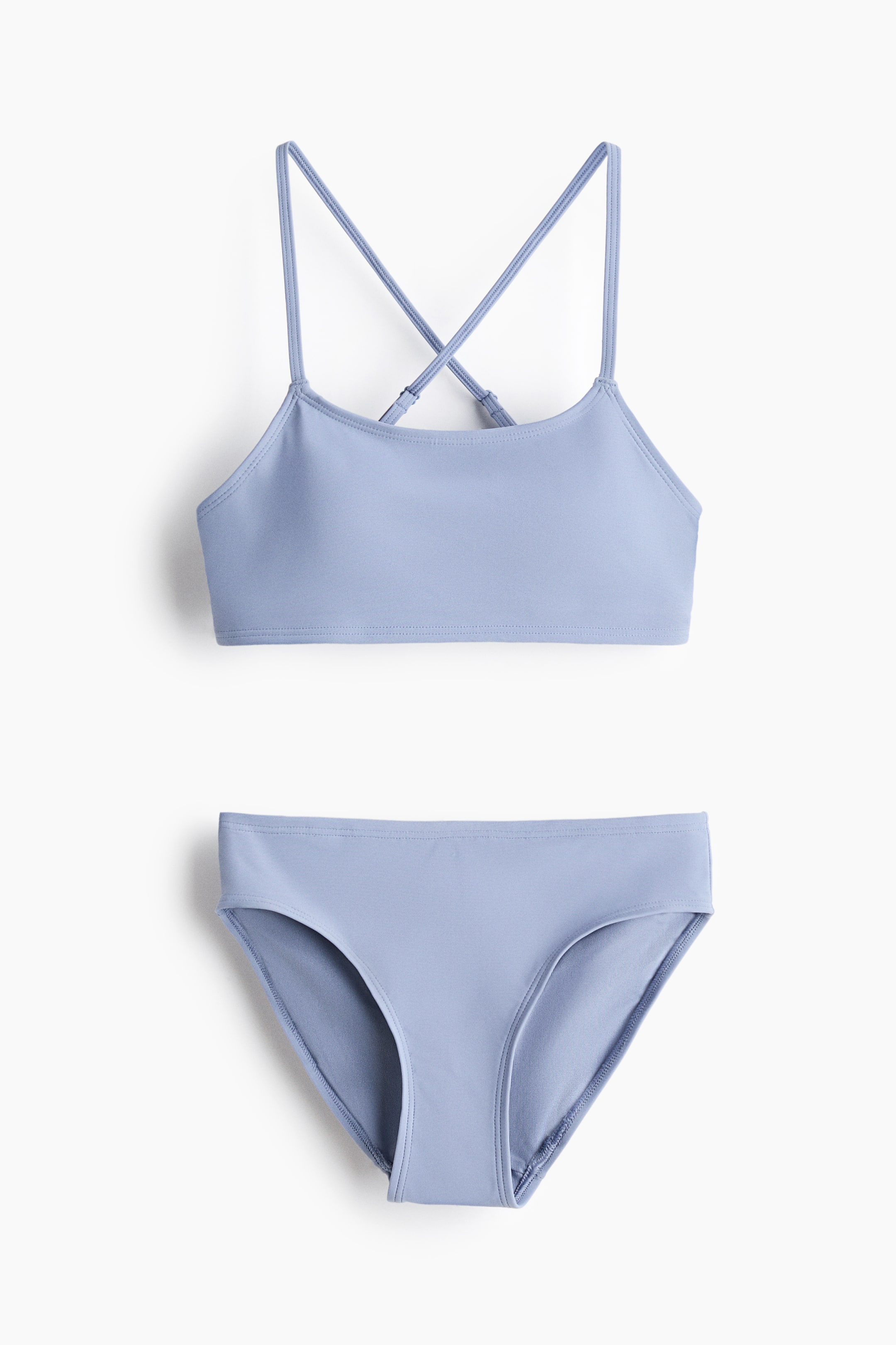 View larger image: A light blue two-piece swimsuit is being displayed, featuring a bralette-style top with thin straps crossing at the back and classic bikini briefs.