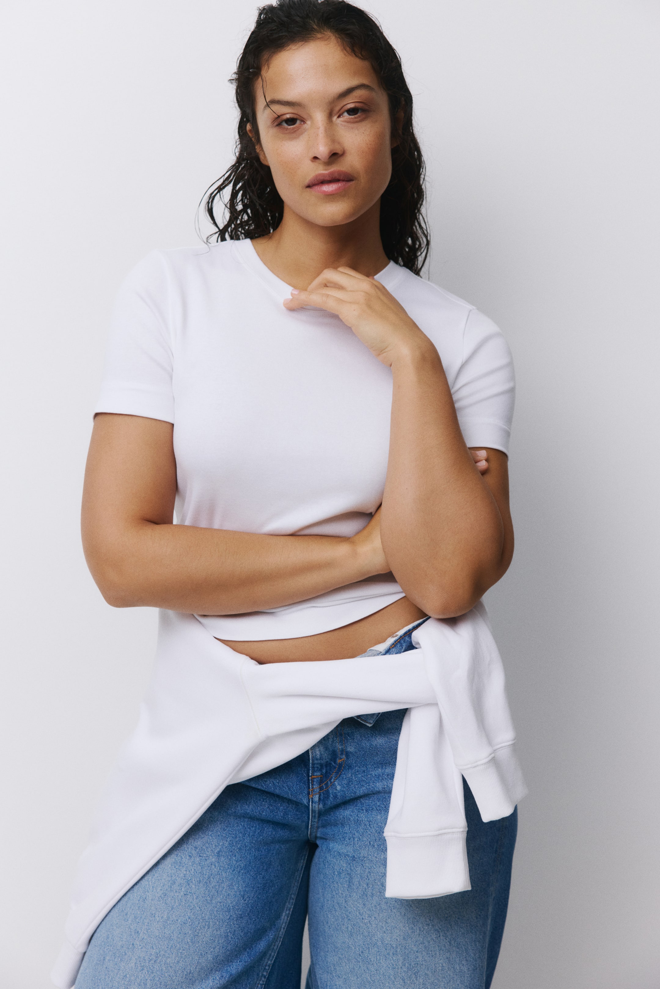 查看大圖: 一件白色短袖圓領T恤被穿著，從正面展現出合身的輪廓。一件白色運動衫，帶有羅紋袖口，繫在腰間。