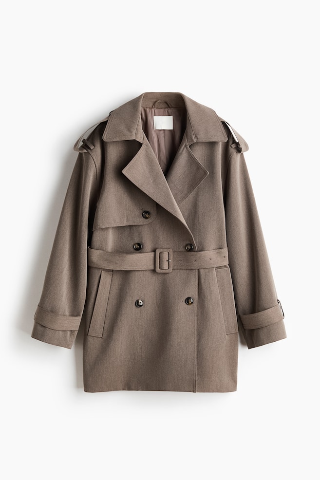 Ein taupefarbener kurzer Trenchcoat präsentiert sich mit einer zweireihigen Vorderseite mit dunklen Knöpfen, breiten Kerbrevers und Schulterklappen. Er verfügt über eine taillierte Passform mit einem rechteckigen Gürtelverschluss, verstellbaren Manschettenriemen und schrägen Leistentaschen. - 1