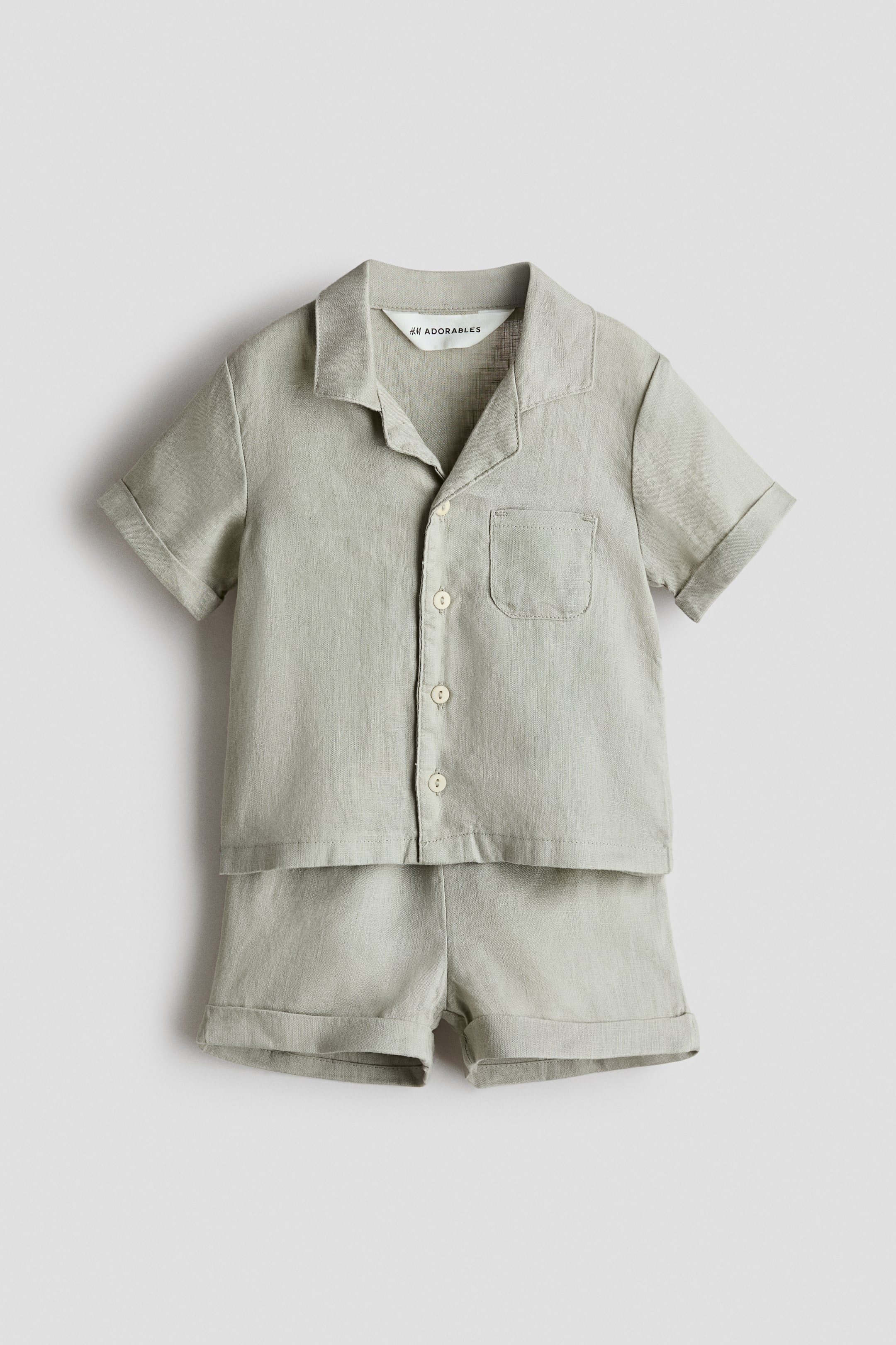 Ampliar la imagen: La parte frontal de un conjunto de dos piezas en verde claro con textura presenta una camisa de manga corta con cuello resort, tapeta de botones al frente, bolsa de parche en el lado izquierdo del pecho y mangas dobladas. El short a juego muestra dobladillos con vuelta.