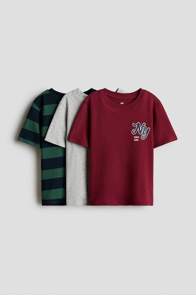 Three cotton jersey t-shirts are overlapping in a front-facing display. The foremost t-shirt is burgundy, featuring a round, rib-trimmed neckline and a small "NY Since 1986" graphic on the chest, while the middle t-shirt is light grey and the back t-shirt is displaying dark green and navy horizontal stripes. - 1