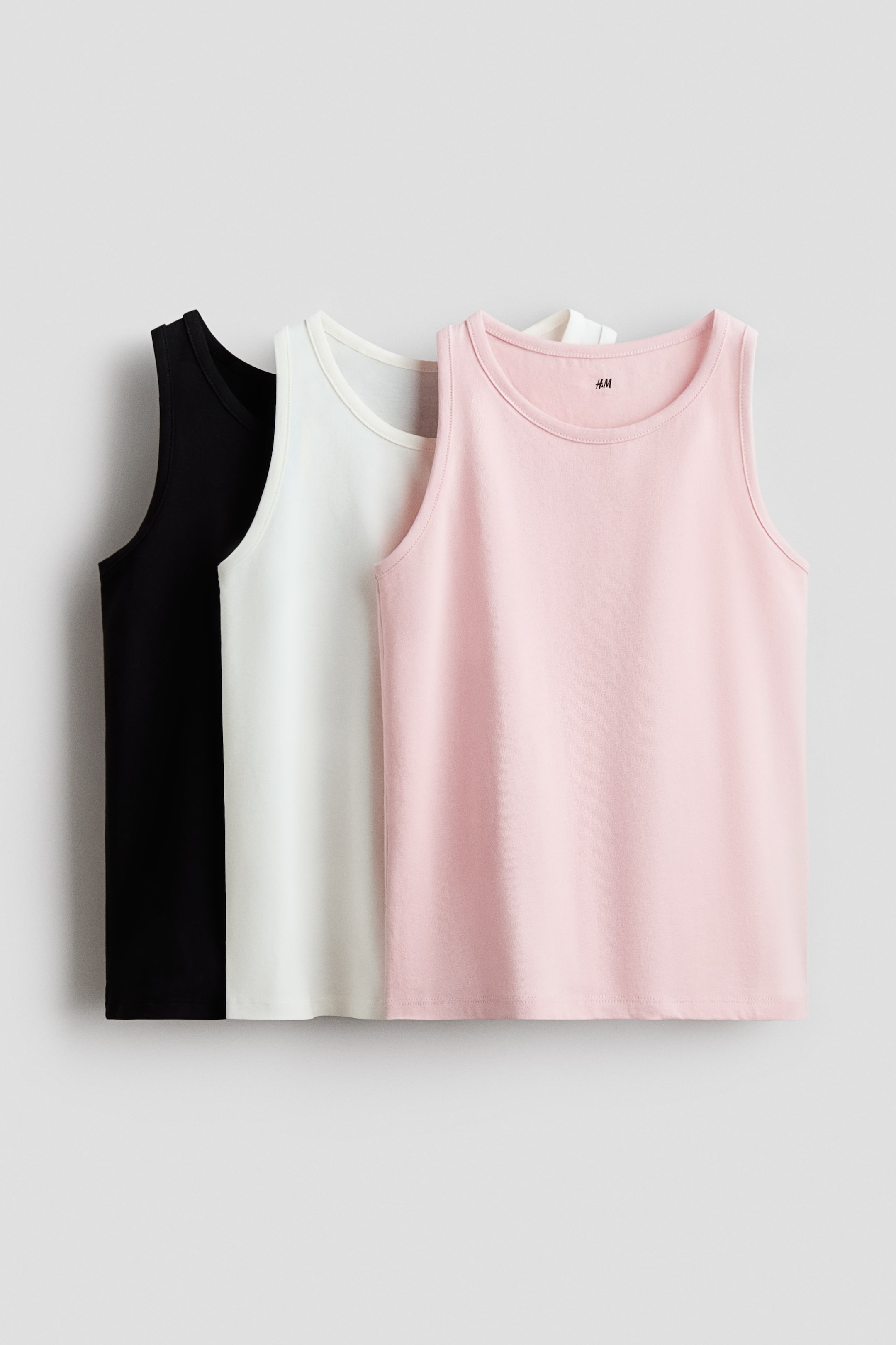 Agrandir l'image: Trois débardeurs sont présentés, superposés de l'avant vers l'arrière en rose, blanc et noir. Chaque débardeur présente un col rond et un design sans manches avec des bords gansés au niveau du col et des emmanchures.