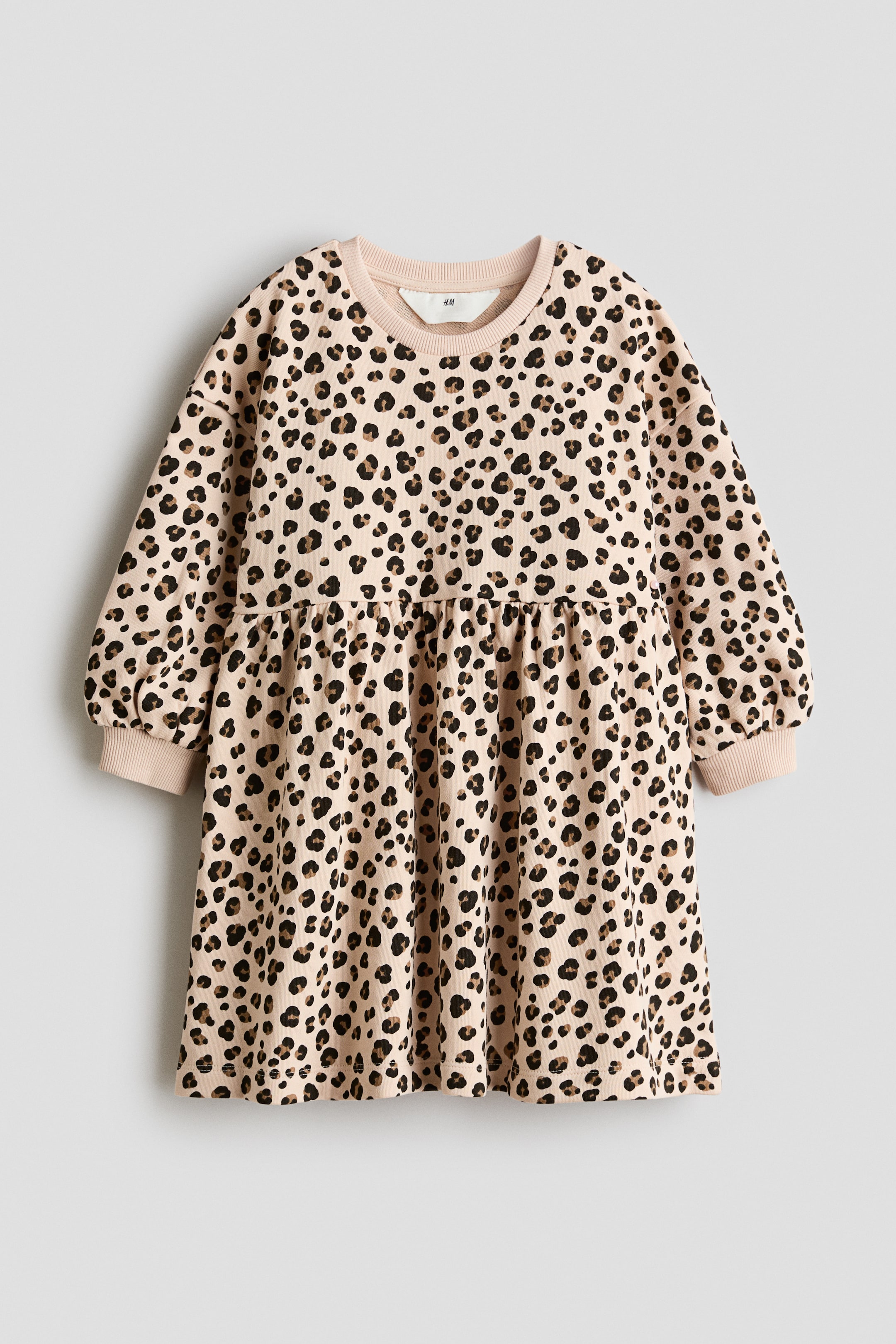 Visa större bild: En beige klänning med leopardmönster ligger platt, vänd framåt, och visar en rund ribbad halsringning och långa ärmar med ribbade muddar. Midjelinjen visar rynkor, vilket skapar en full kjol.