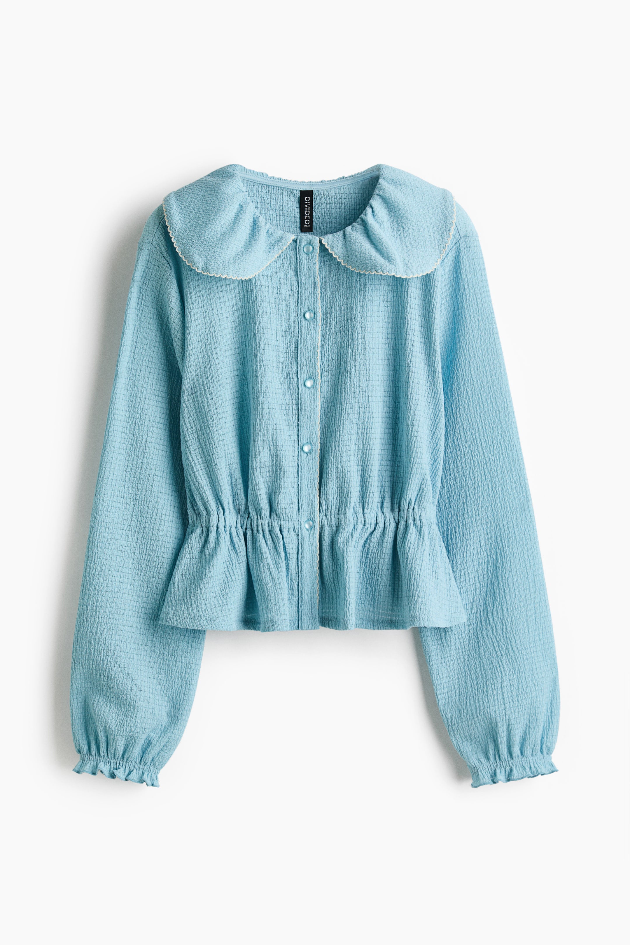 View larger image: FRONT: a light-blue top in textured jersey features a picot-trimmed Peter Pan collar and a button band. It has gently dropped shoulders, long sleeves with elastication and overlocked edges at the cuffs, and covered, gathered elastication at the waist that creates a flared peplum.